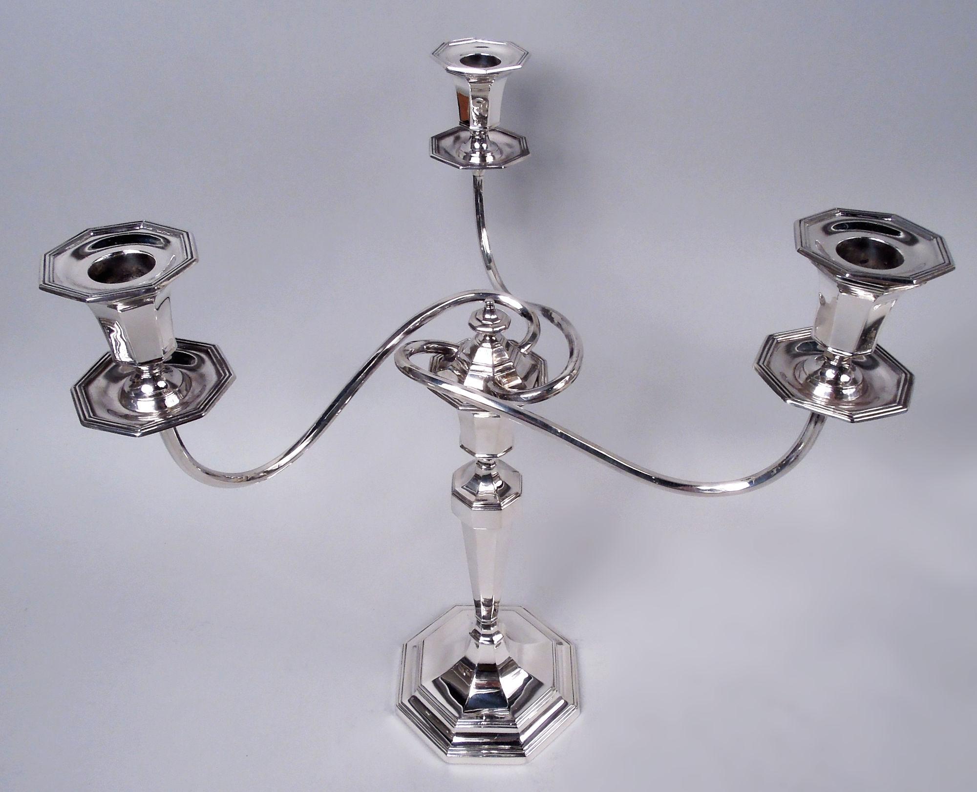 Pair of George V sterling silver candlesticks. Made by Crichton Brothers in London in 1926-28. Each: Tapering columnar shaft on stepped foot; urn socket has domed cover with vasiform finial, and is mounted with three wraparound arms, each