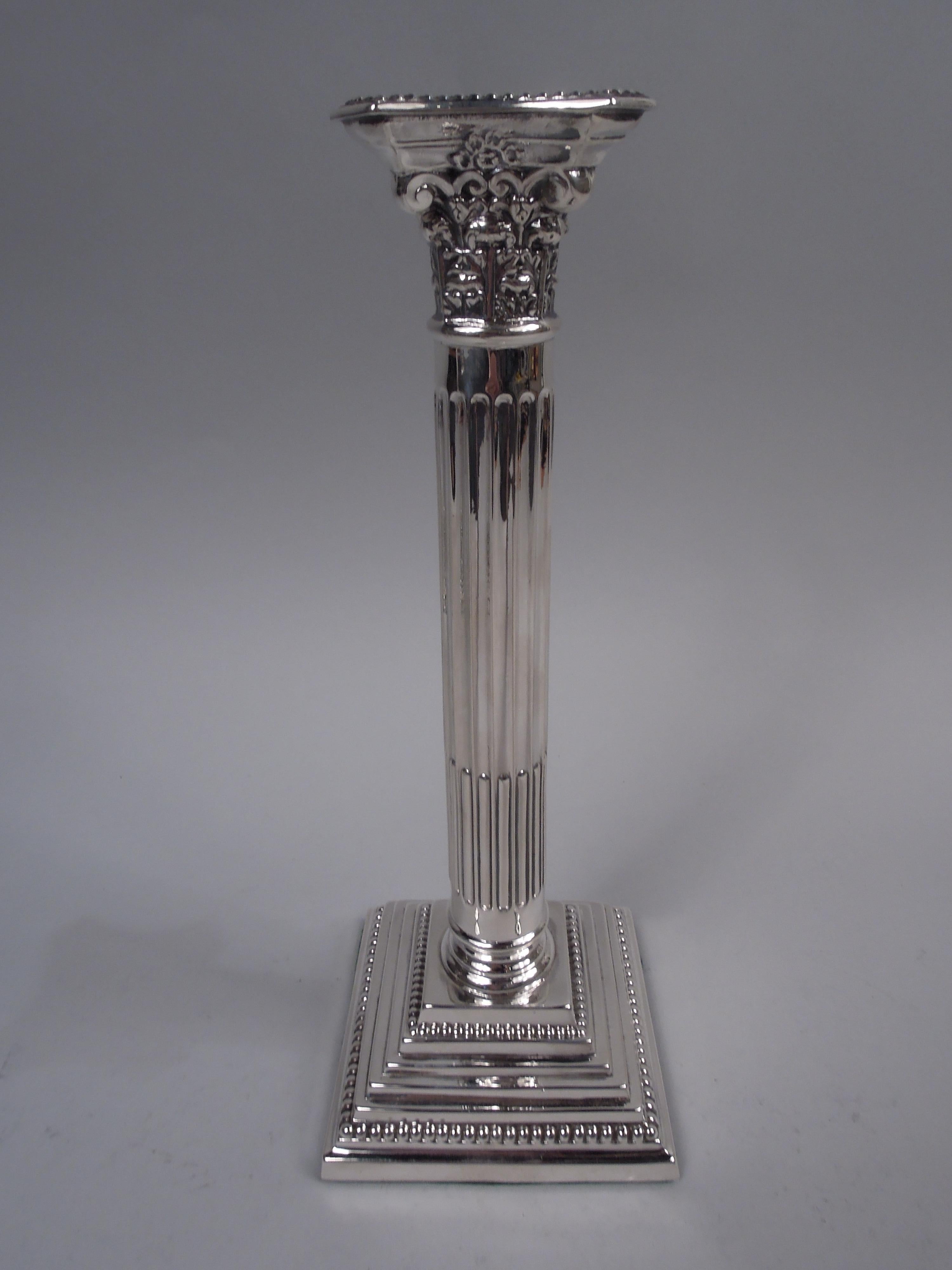 Paire de chandeliers néoclassiques anglais en argent sterling, 1933. Chaque : Colonne traditionnelle avec un arbre à cannelures sur une base carrée étagée. Chapiteau corinthien composite aux côtés concaves et à la bobèche amovible. Perles.