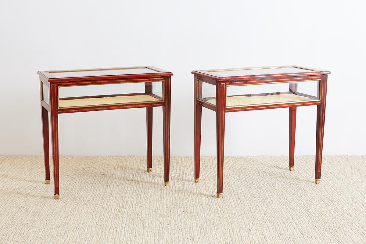 Exquisite matching pair of English vitrines or display tables also known as Bijouterie tables. Features a beautifully carved mahogany frame with a delicate brass thread inlay accenting the entire case and legs. The case has beveled glass on all
