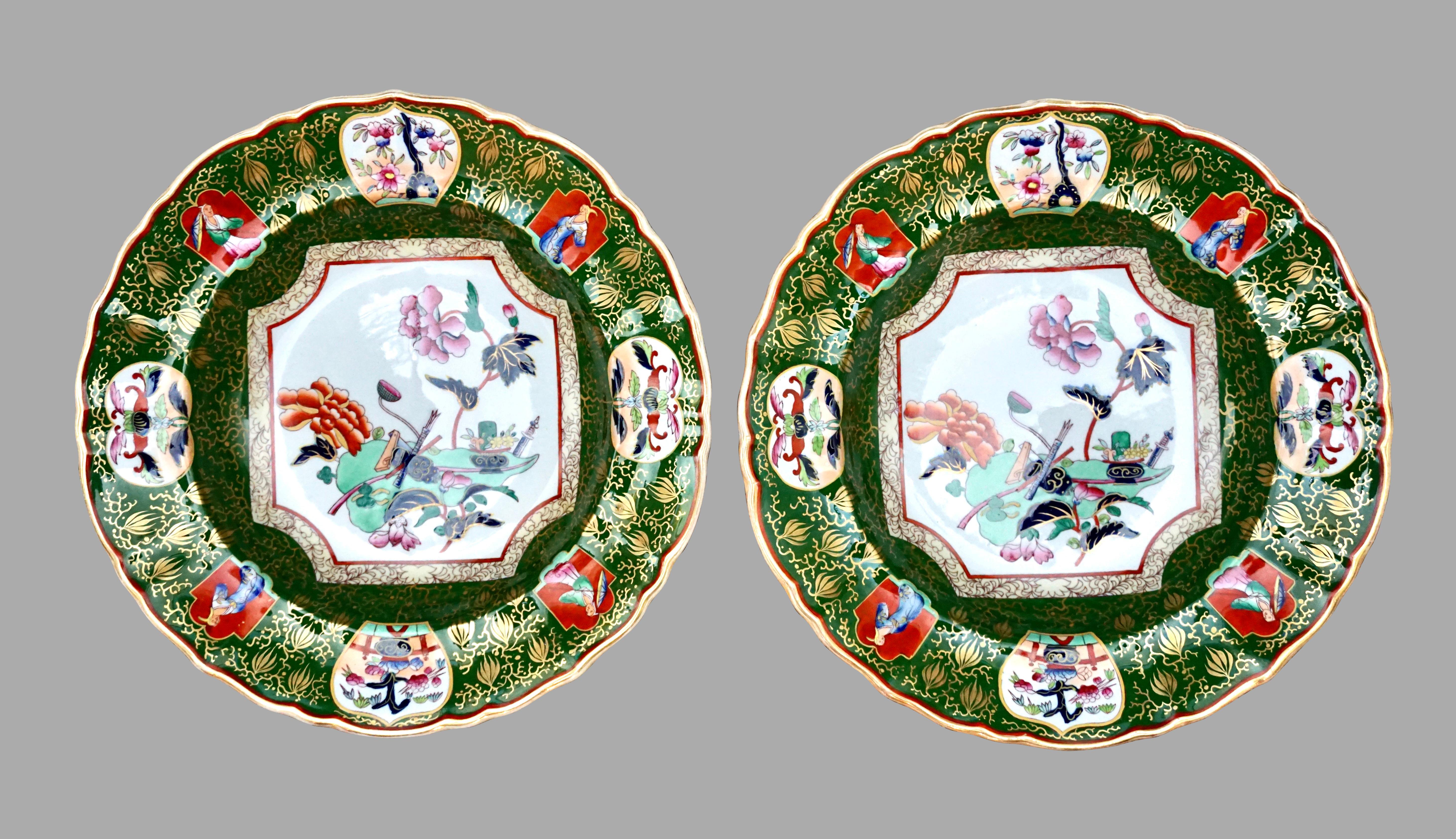 An exuberant pair of English Asian influenced Ironstone bowls hand decorated with green, rose, orange and blue garbed figures in perimeter cartouches, 2 with parasols, further decorated with flowers, trees and plants, all on a gilt-decorated green