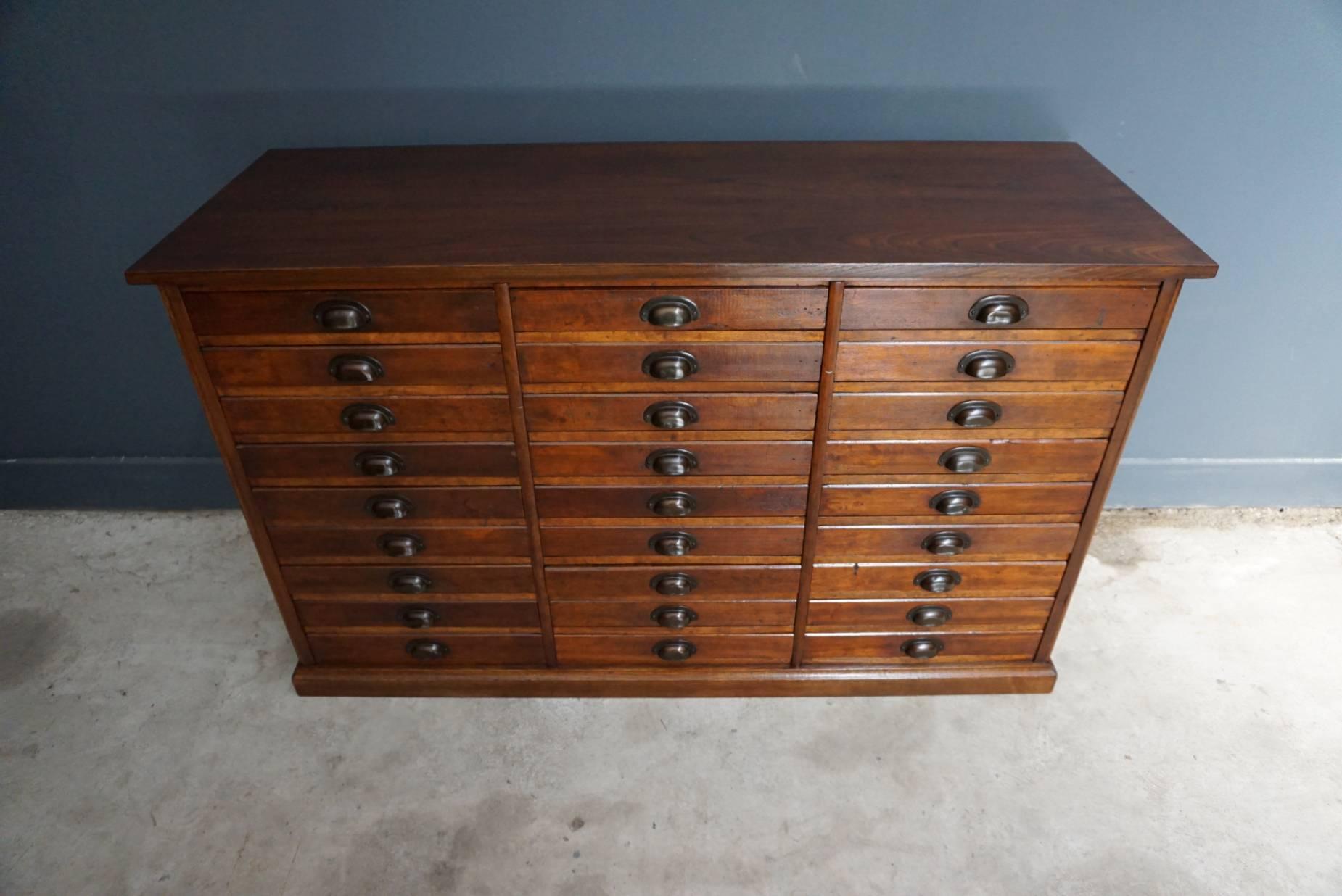 This oak apothecary cabinet was designed and made circa 1950 in England. It features 27 drawers with metal cup handles. The inside of the drawers measure: 33 x 44 x 5.8 cm, some have dividers and some don't. We have two pieces of this item