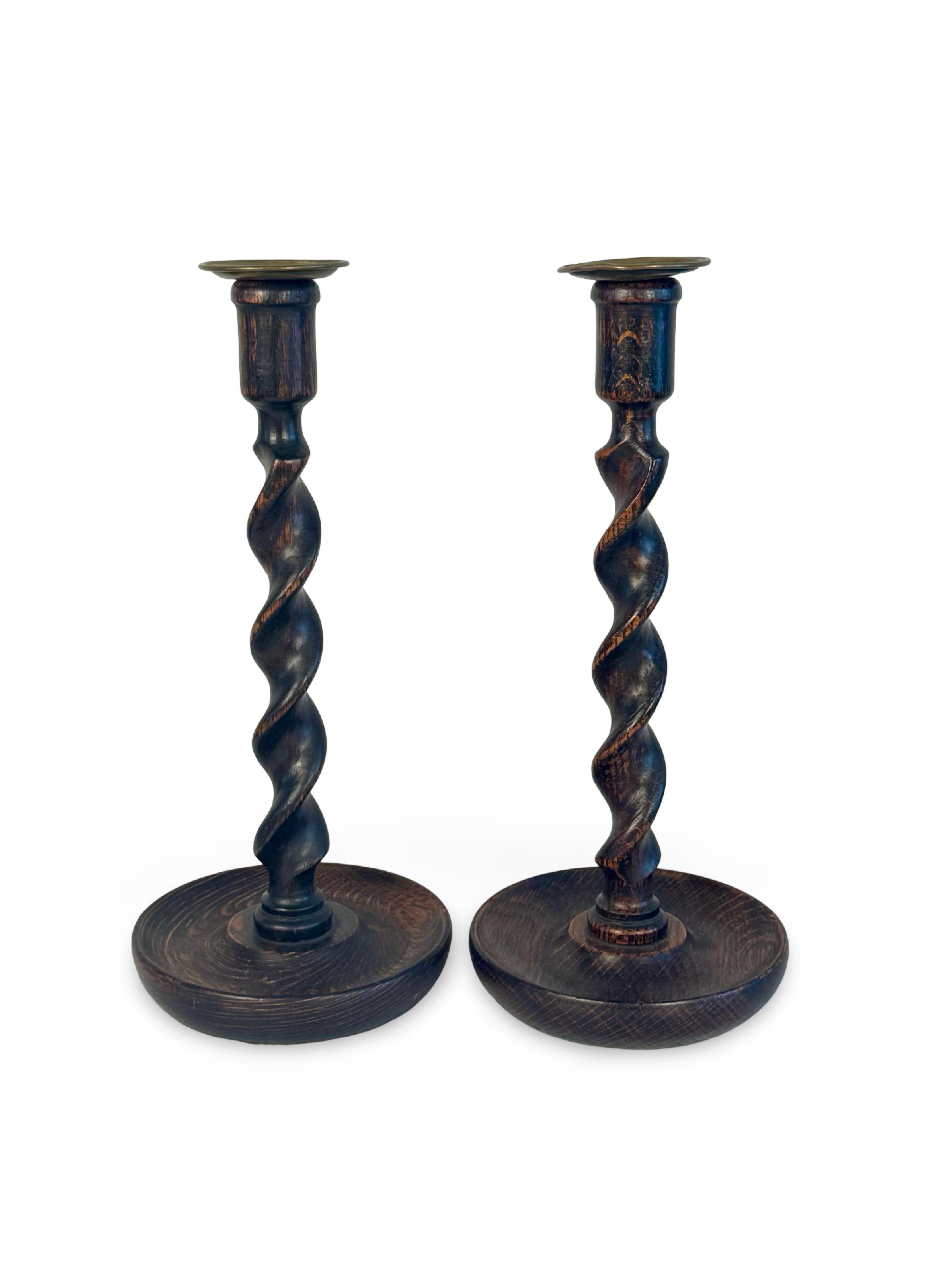Bellissima coppia di candelieri inglesi in legno di quercia tornito, i cui steli a spirale poggiano su basi a forma di piatto finemente intagliate, sormontate da bobeches in ottone. Fine del XIX o inizio del XX secolo.