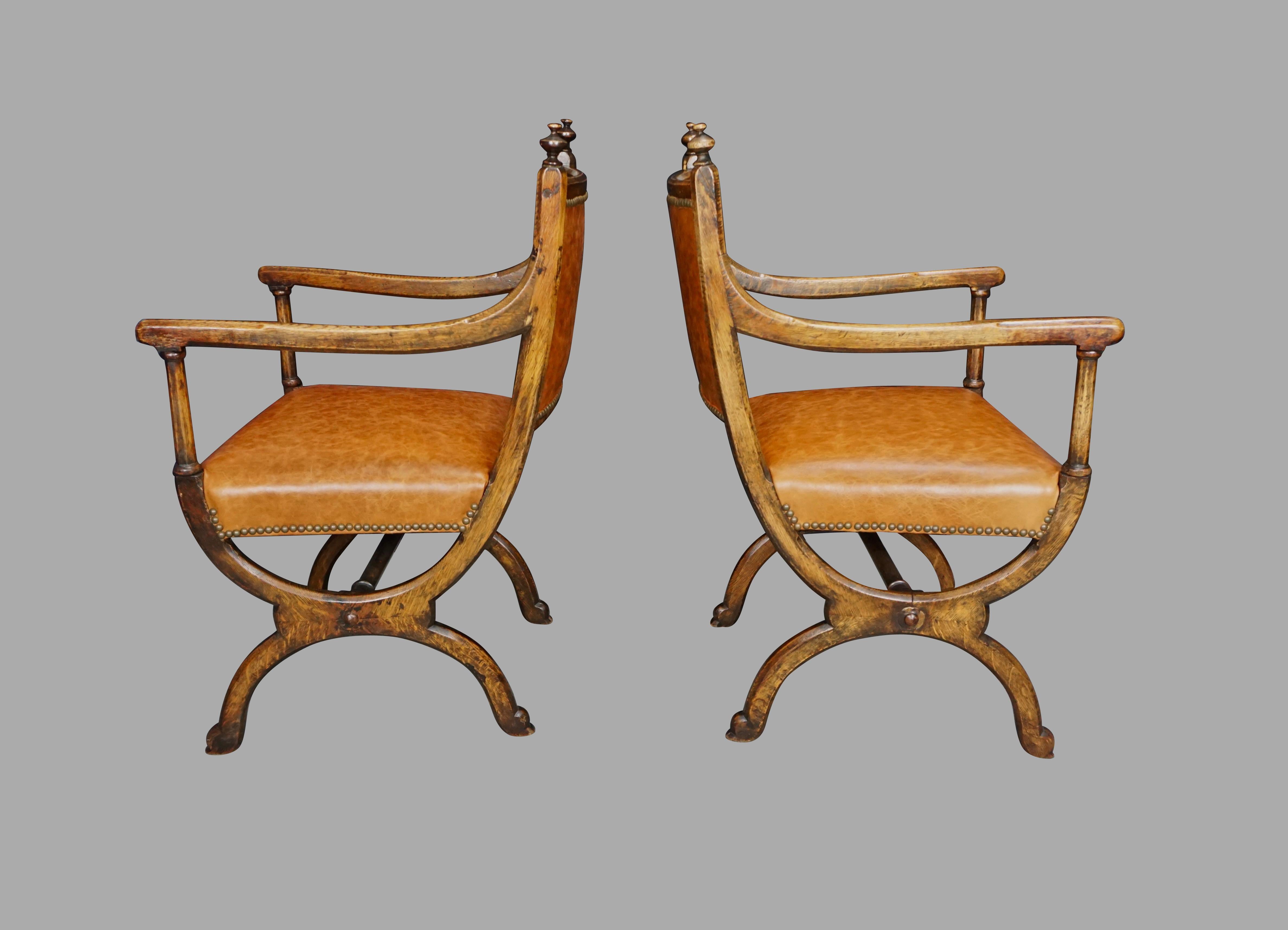 A pair of English oak Gothic Revival Curule armchairs after a design by A.W.N. Pugin, the crest rail with turned finials, the faceted arms transitioning to hexagonal columns ending in ring turned elements connected to curved legs joined by a central