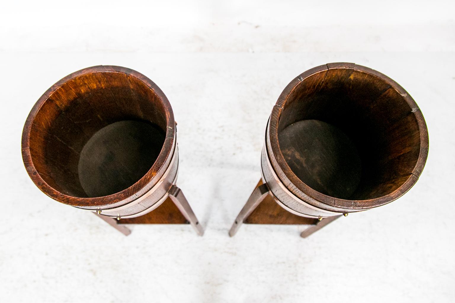 This pair of oak planter stands has solid brass copper studded bands supported by tripod legs joined by a triangular shelf. 
   