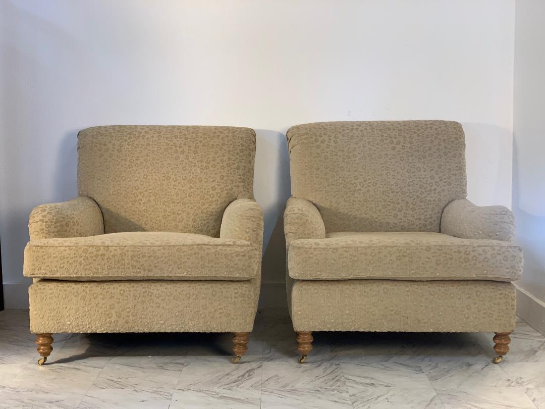 Pair of English oversized upholstered lounge chairs. Original upholstery, solid wooden legs with brass casters to the front legs.