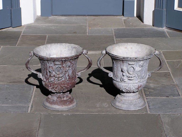 Pair of English lead poly chromed garden urns each with flanking scrolled handles, cherub and acanthus foliage, and terminating on circular dome plinths, Early 19th century. 
Urns are 17.5