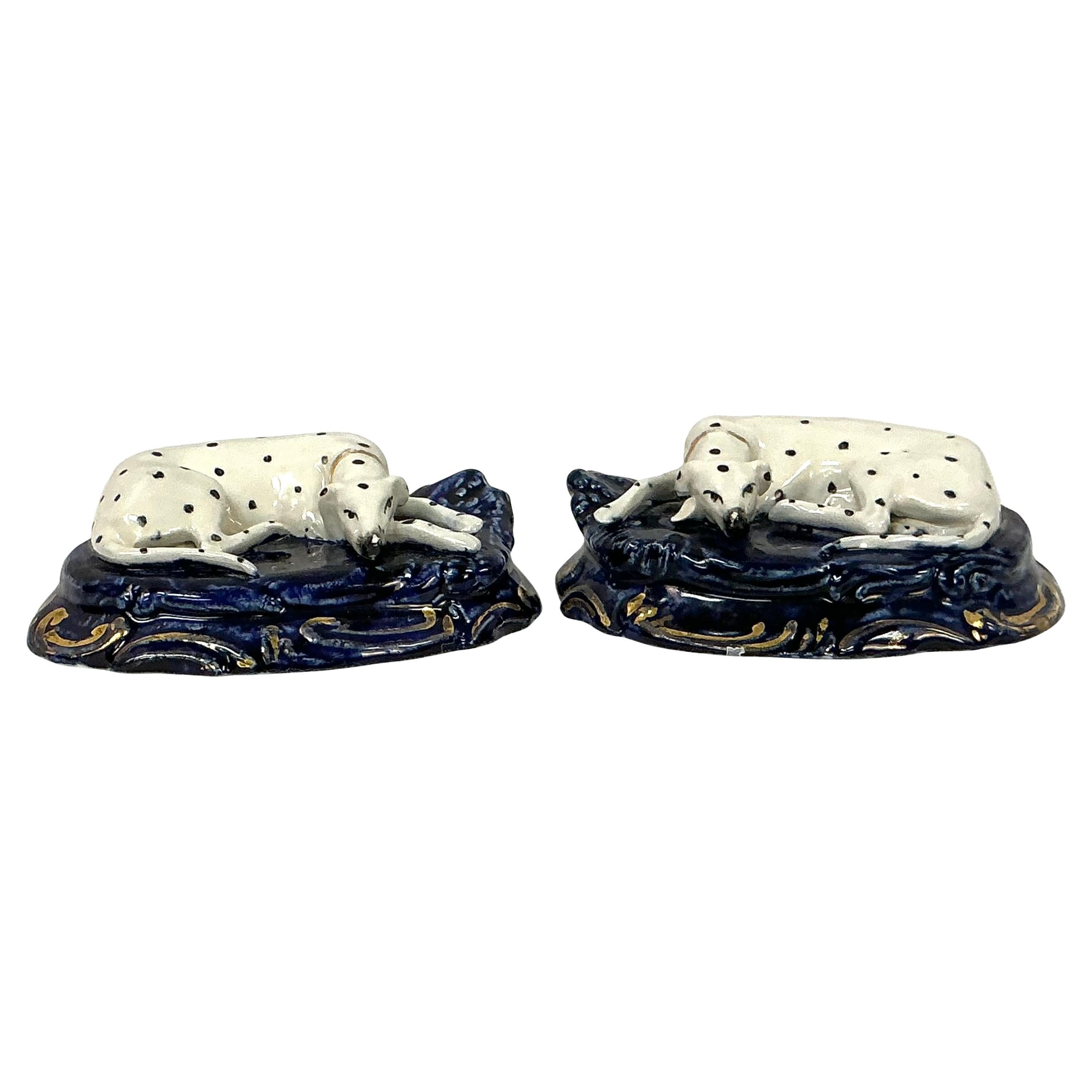 Pair of English Porcelain Hand-Painted Staffordshire Dalmatian Dogs Figurines. These figurines feature recumbent Dalmatian dogs with expressive faces and detailed features resting on a cobalt blue base with gold accents. They would be lovely as as