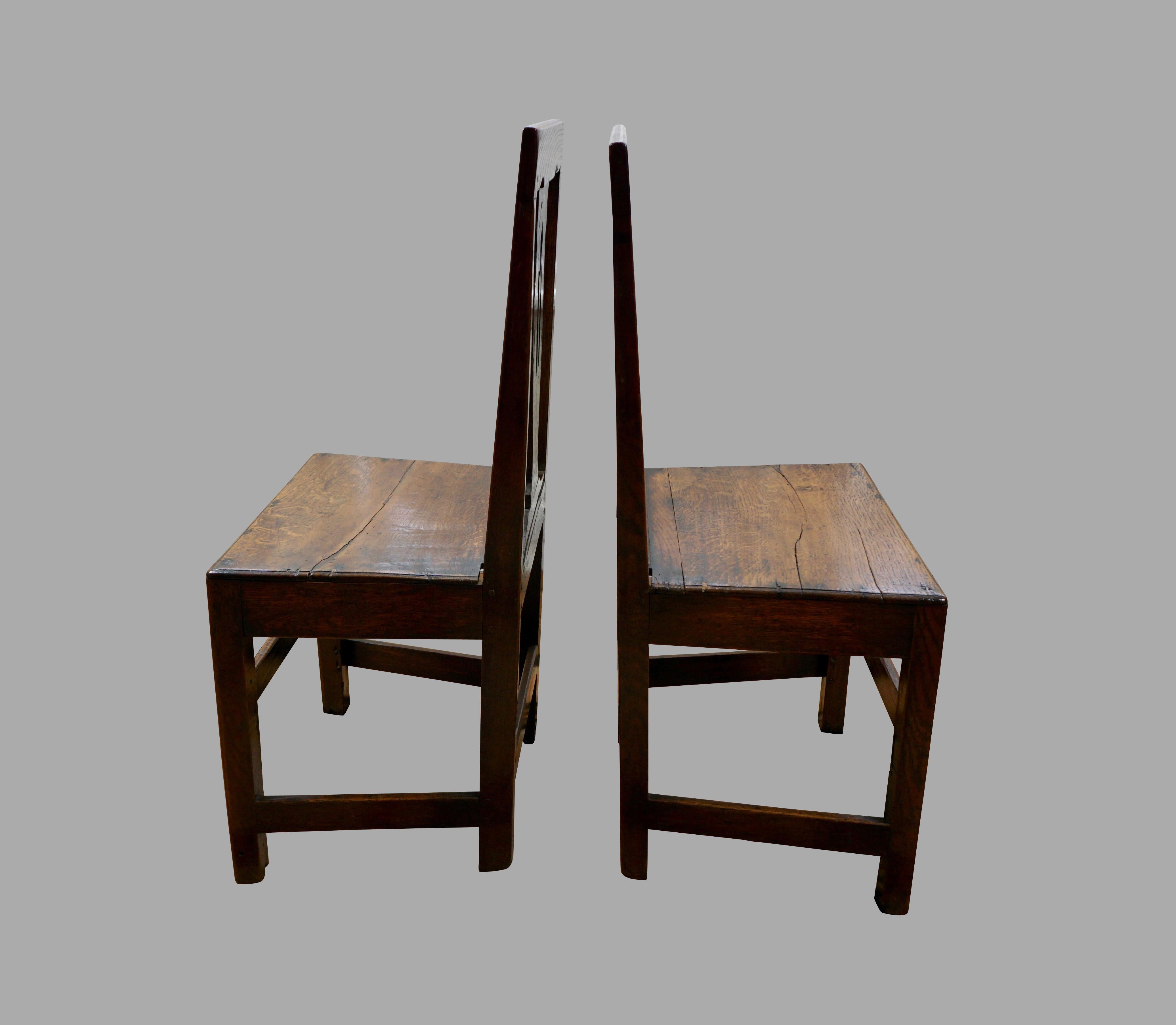 A charming pair of English provincial oak side chairs with open splats above solid seats supported on straight legs joined by box stretchers, Circa 1750. Slight variations in height.