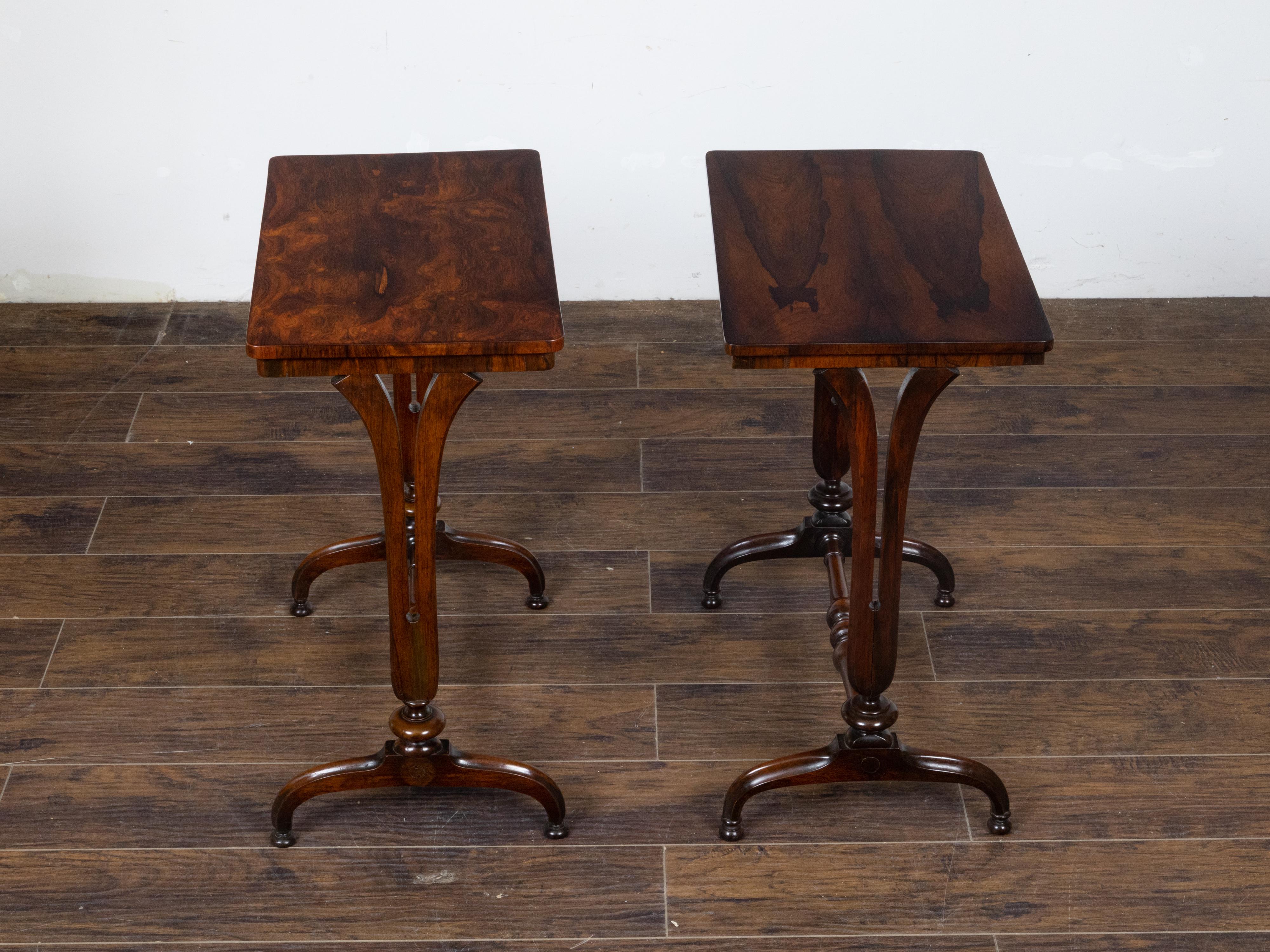 A pair of English Regency period wooden console tables from the 19th century with veneered top, curving legs, arching feet and spindle shaped cross stretchers. This pair of English Regency period wooden console tables, dating back to the 19th