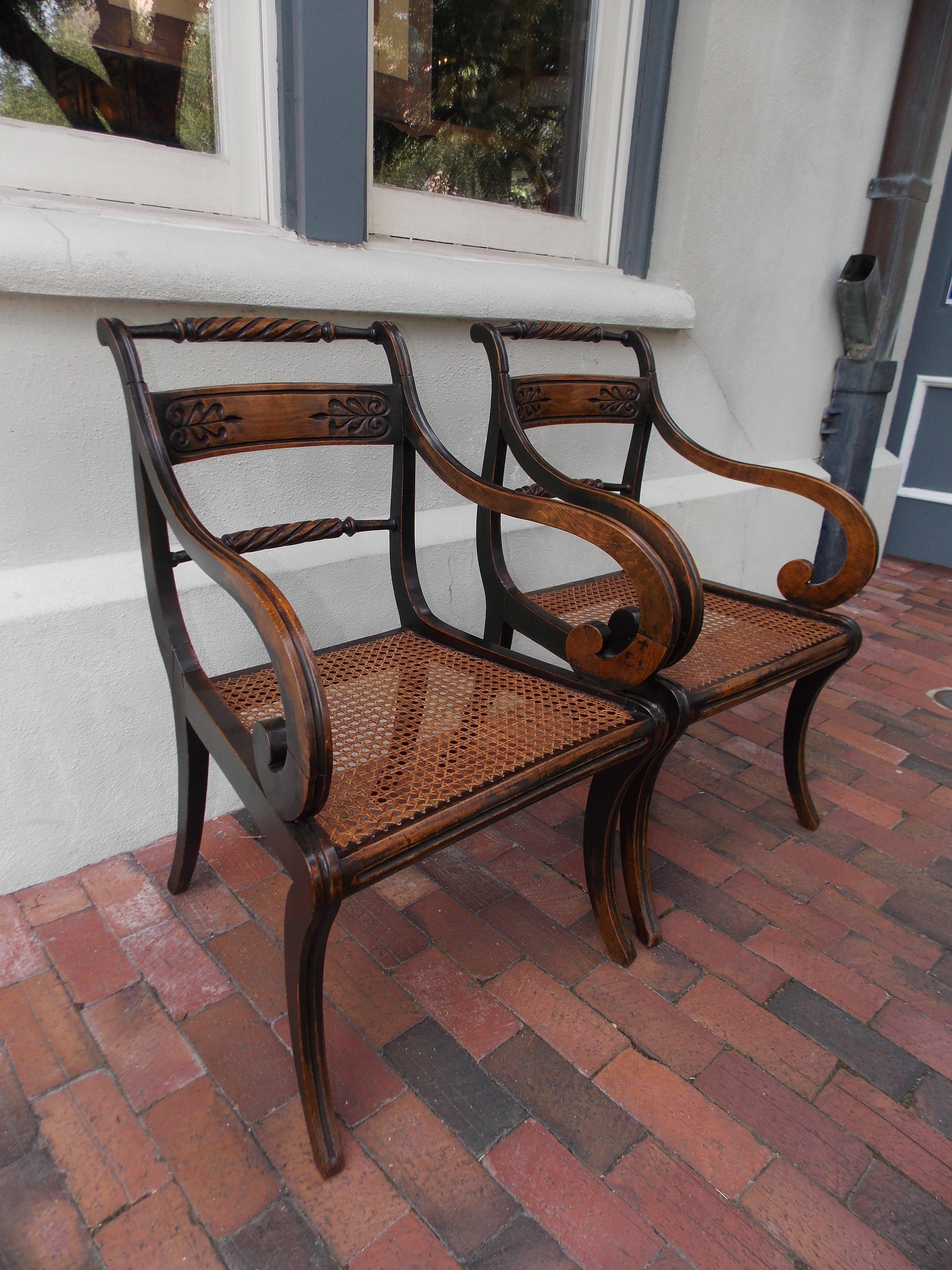 Pair of English Regency black lacquered arm chairs with a carved spiral ringed bulbous crest, flanking filigree splat backs, sweeping carved scrolled arms, cane hole seats, and terminating on the original splayed legs, Early 19th century.