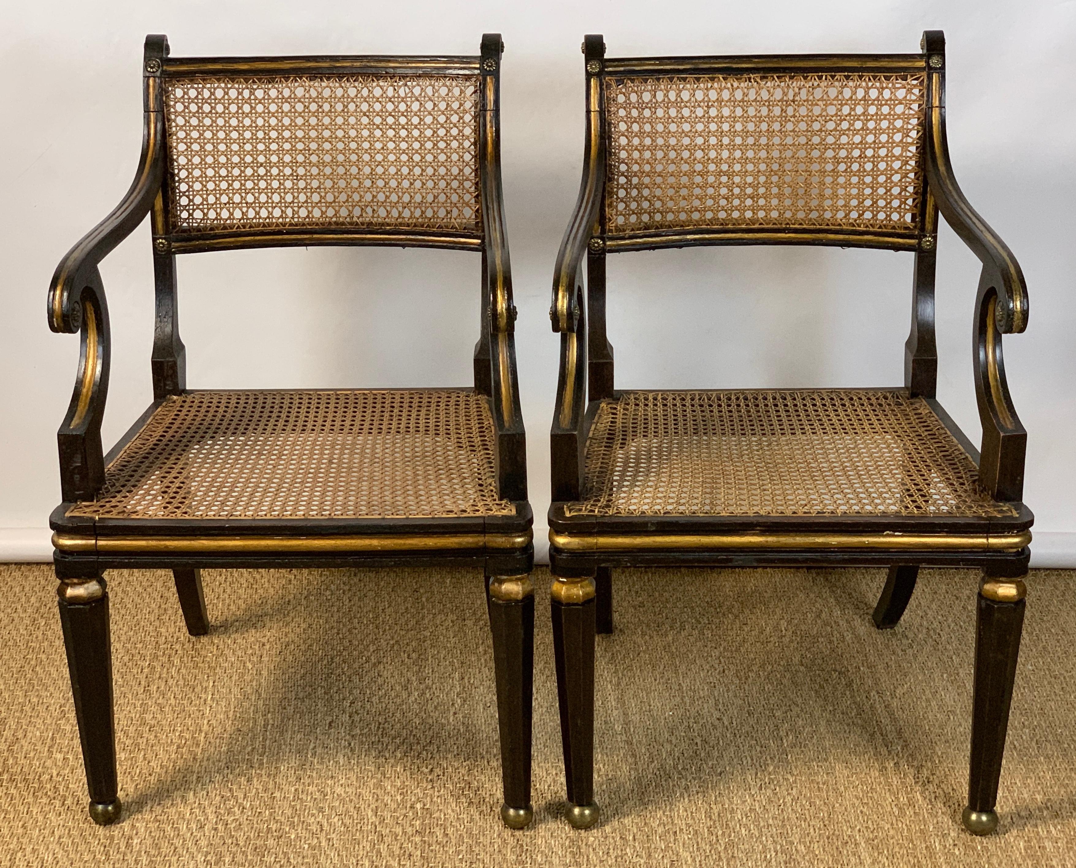 An elegant pair of early 19th century English ebonized and gilt decorated Regency period armchairs featuring cane backs and seats accented with gilt bronze mounts resting on octagonal tapering legs terminating in cast bronze ball feet with later