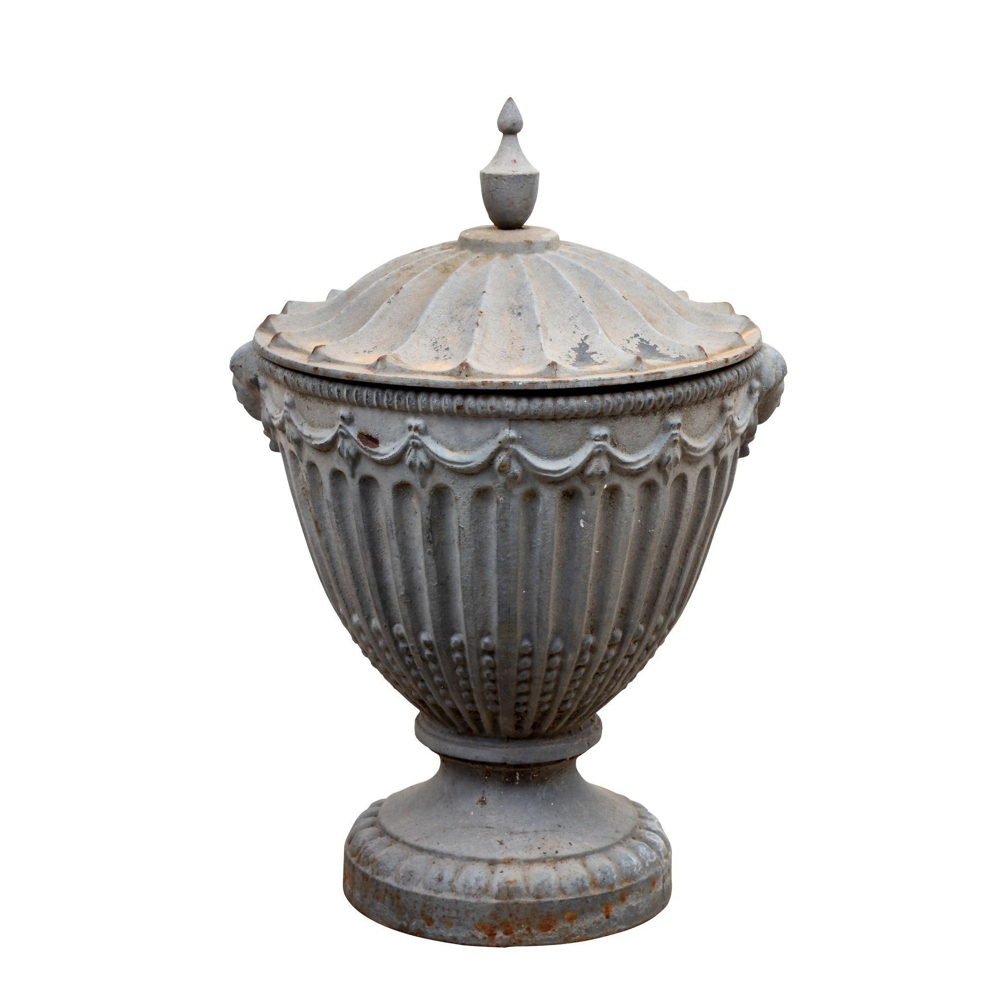 Exuding timeless elegance, this exceptional pair of lidded urns hails from 19th century England, possibly originating from an esteemed estate or country manor. Crafted during the 1860s, these ornate urns are painted to imitate lead and boast