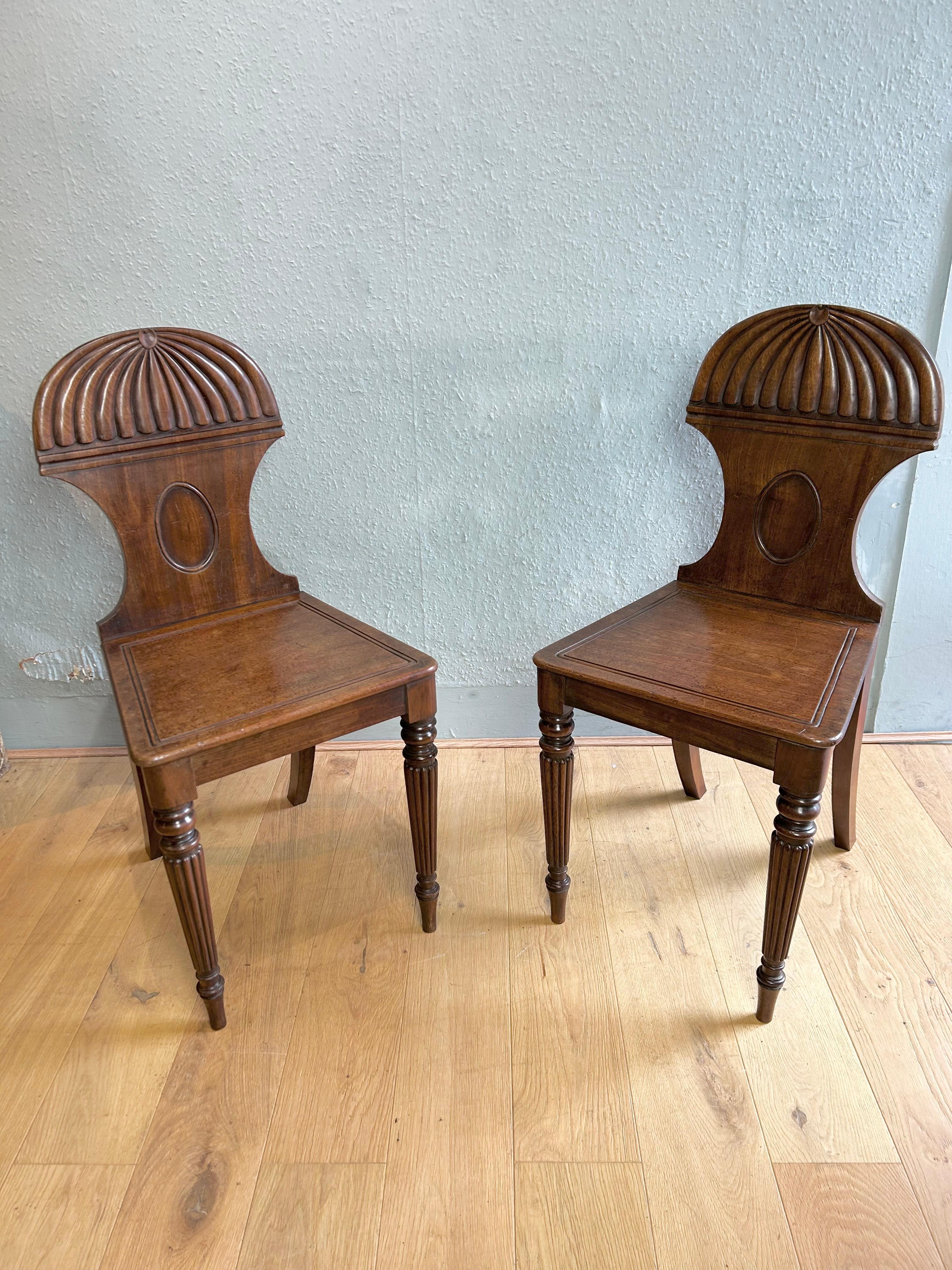 Pair of antique English Regency mahogany hall chairs attributed to Gillows of Lancaster and London circa 1815 with a classic carved dragooned canopy, moulded seat resting on fine reeded turned legs of typical Gillows design, chairs retain their