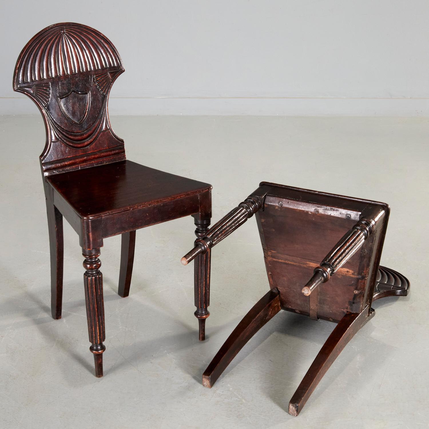 a pair of English Regency mahogany hall chairs, carved back with shield at center, on turned tapered reeded front legs, having rear sabre legs, England, 19th century