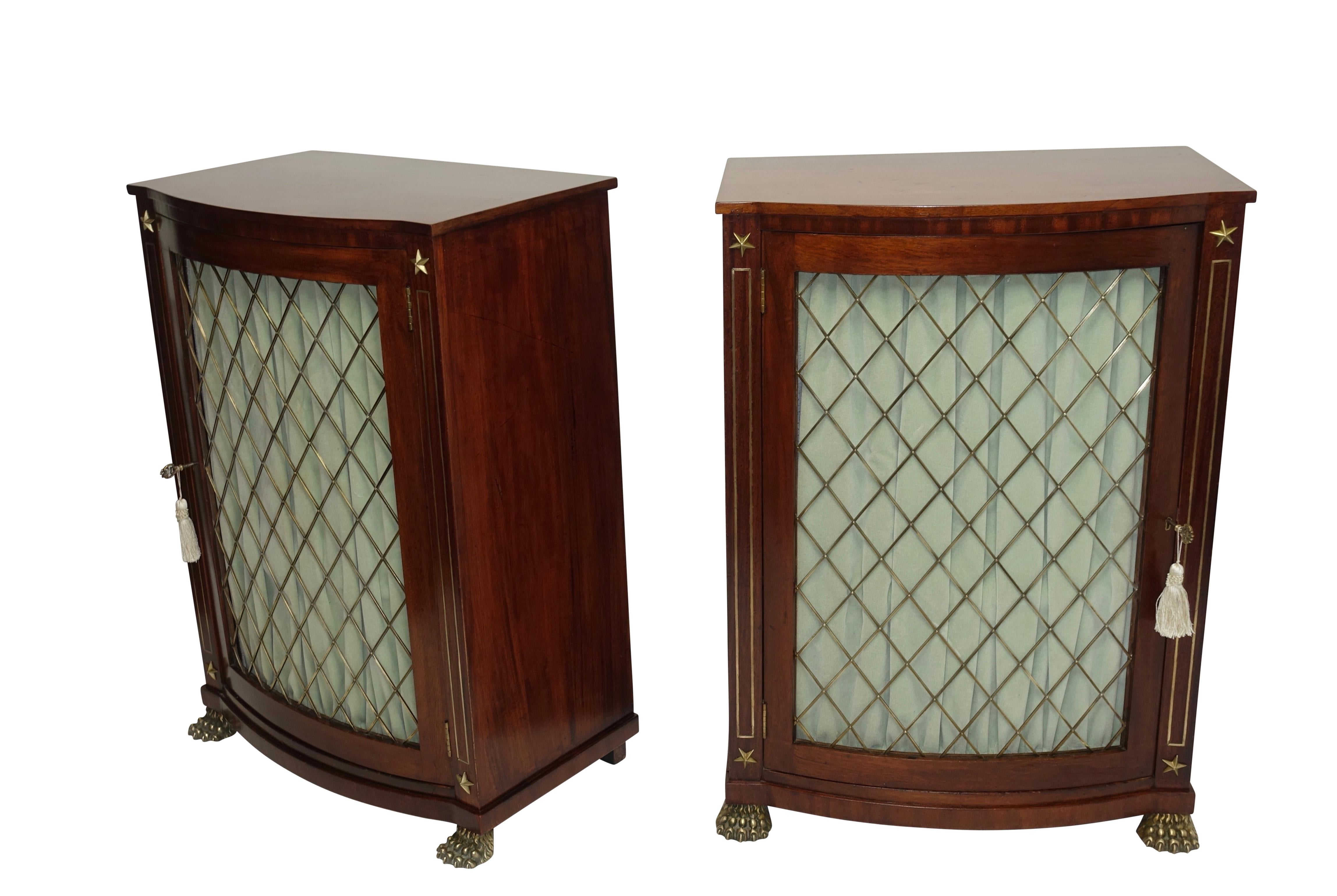 An exceptional matched pair of mahogany Regency period bow front library side cabinets with brass mounts and inlay, applied star decorations, and having original bronze screens. Each cabinet having a single interior shelf. Originally screen was