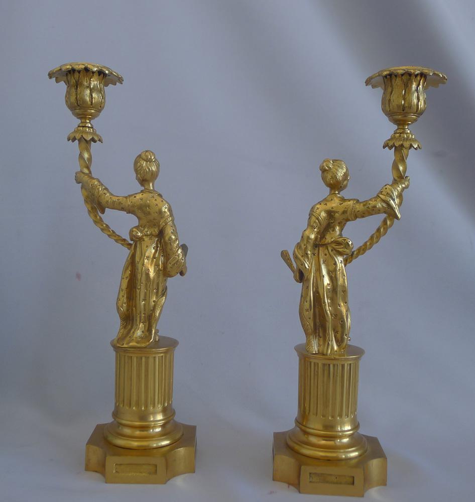 A very attractive true pair of antique English Regency ormolu chinoiserie candlesticks. In the form of oriental women holding up a single candle sconce. Each lady in very finely decorated robes, also hold a fan in their hands. Both set upon fluted