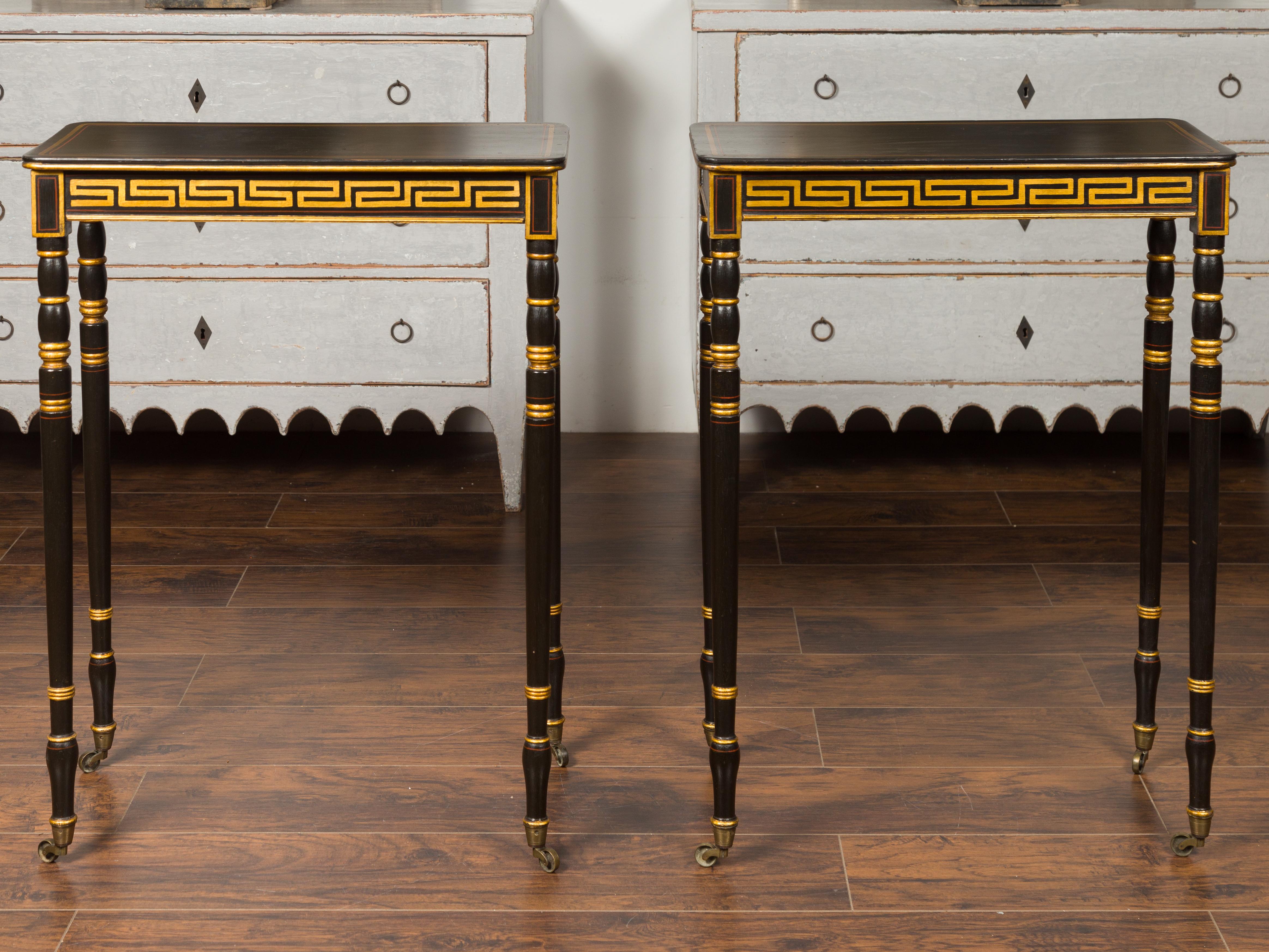 A pair of English Regency period ebonized wood console tables from the early 19th century, with gilded Greek Key friezes. Born in England during the Regency era, each of this pair of console tables features a rectangular top sitting above a stunning