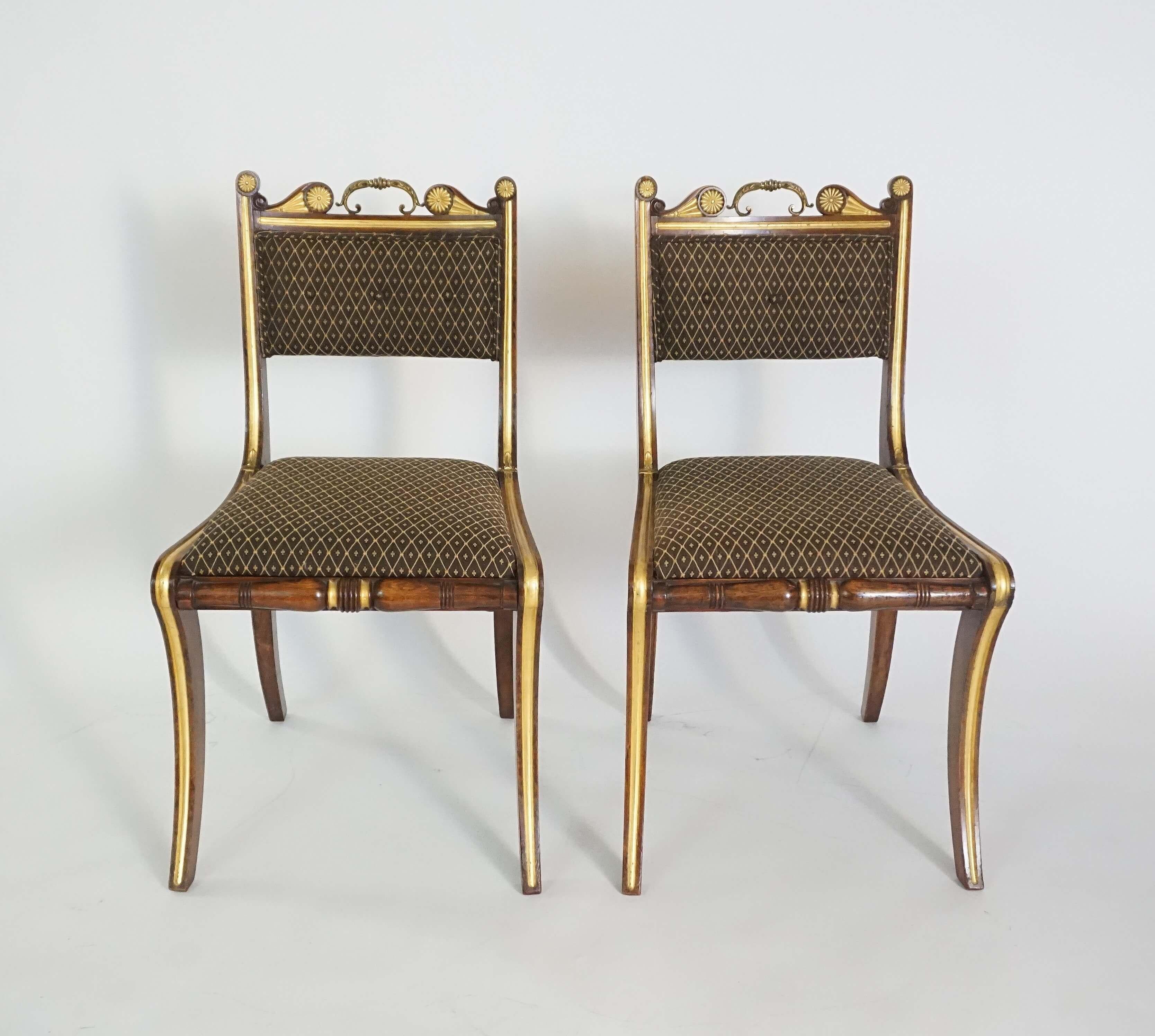 Pair of circa 1815 English Regency period side chairs attributed to renowned cabinetmakers Morel & Hughes having parcel-gilt and gilt-metal mounted rosewood 'klismos-form' frames; the crest-rail with original gilt metal 'butler's pull' above