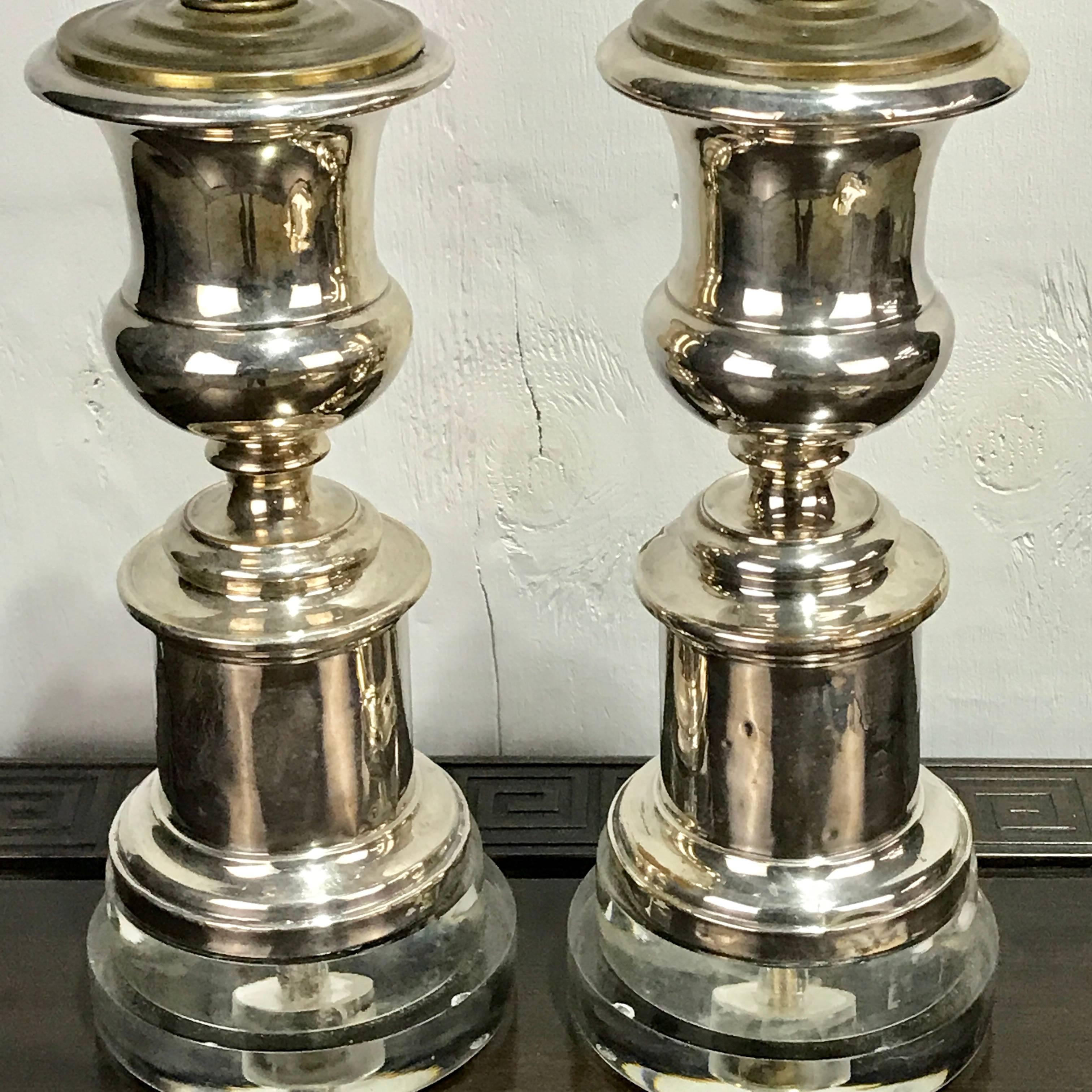 Pair of English Regency silver plated urns now as lamps, each one custom mounted on Lucite pedestal bases. The lamps stand in total height to the socket is 19.5