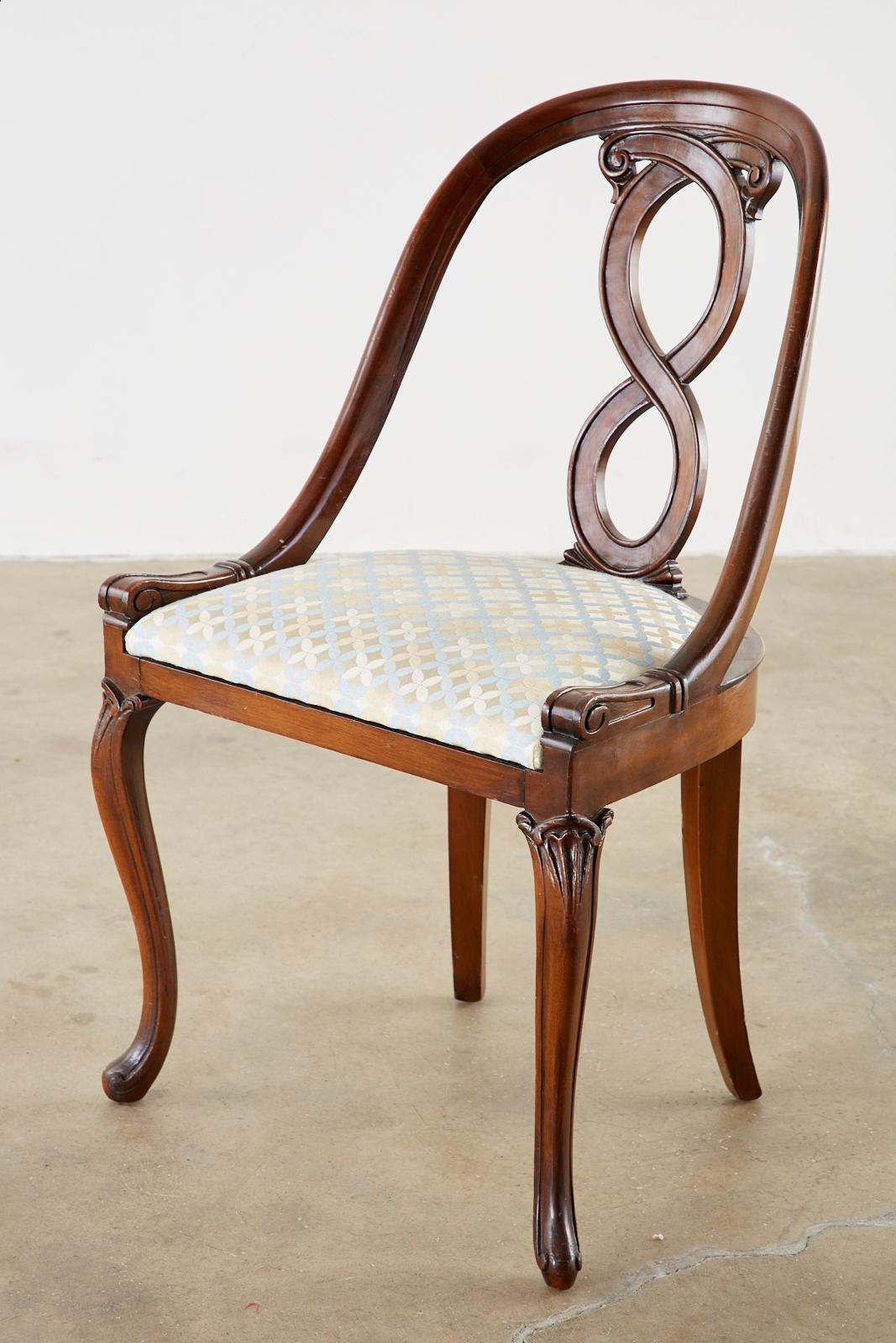 Distinctive pair of English regency chairs featuring a spoon back form. Constructed from mahogany with a carved ribbon design back splat. Supported by graceful cabriole legs in the front. Newer upholstery with a geometric design brocade fabric in a