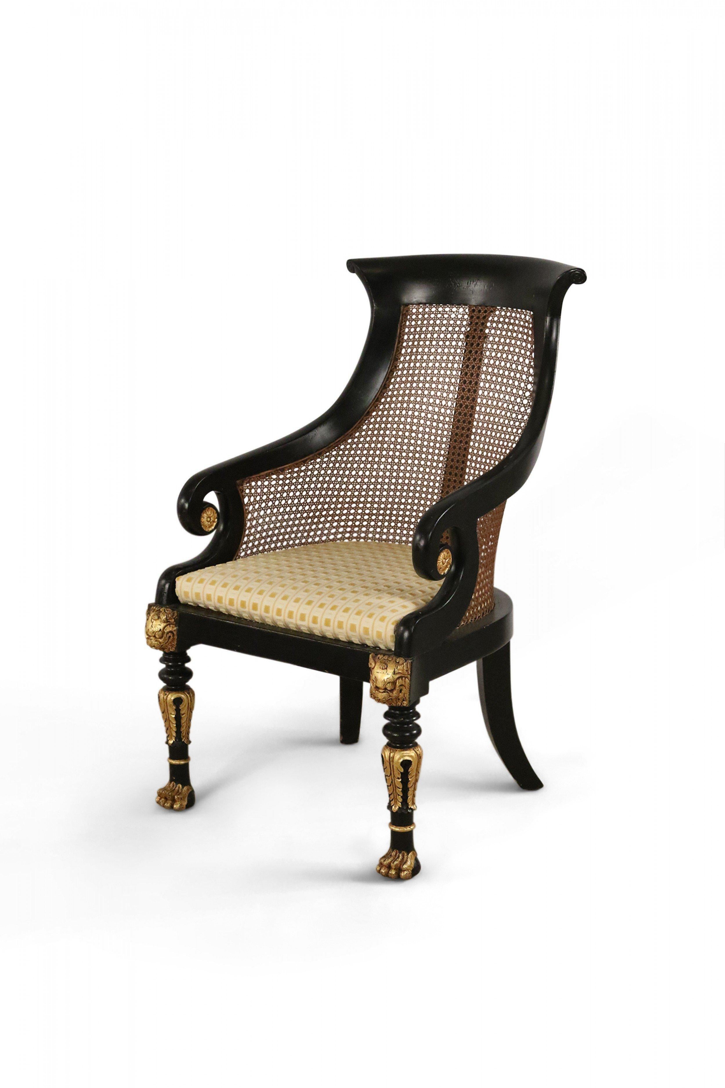 Pair of English Regency style (20th century) armchairs with black and gilt painted wooden frames with carved detail, cane seat backs, light yellow and gold seat upholstery, and carved paw feet. (Priced as pair).