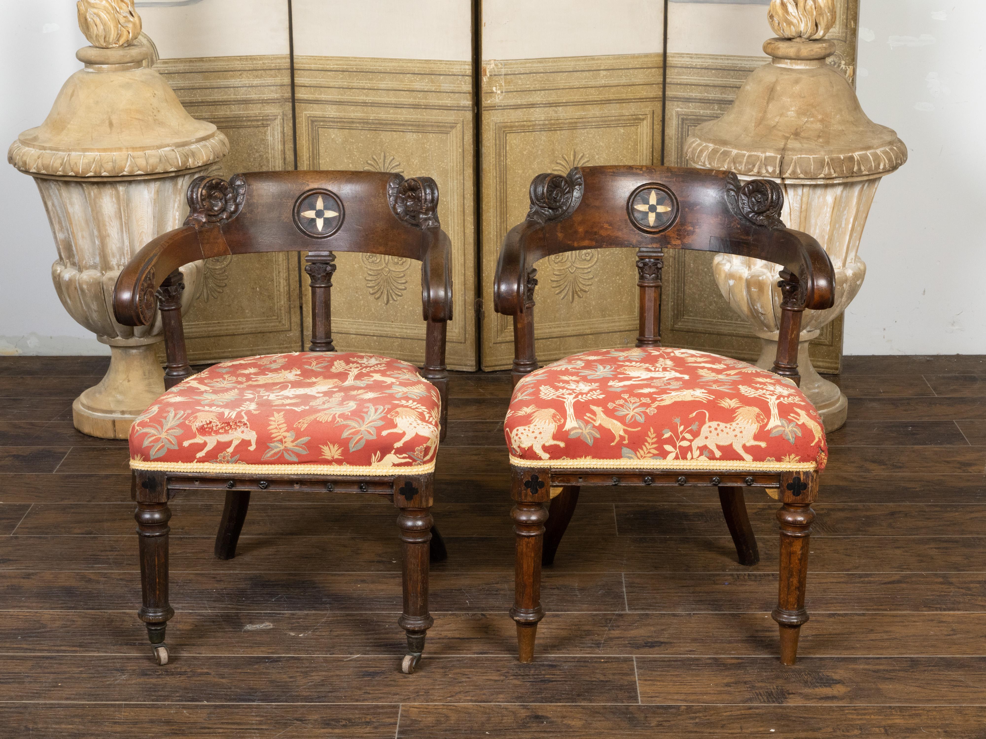 A pair of English Regency style oak Klismos chairs from the 19th century, with carved scrolling decor, geometric inlay and old fabric. Created in England during the 19th century, each of this pair of Regency style Klismos chairs features a horseshoe