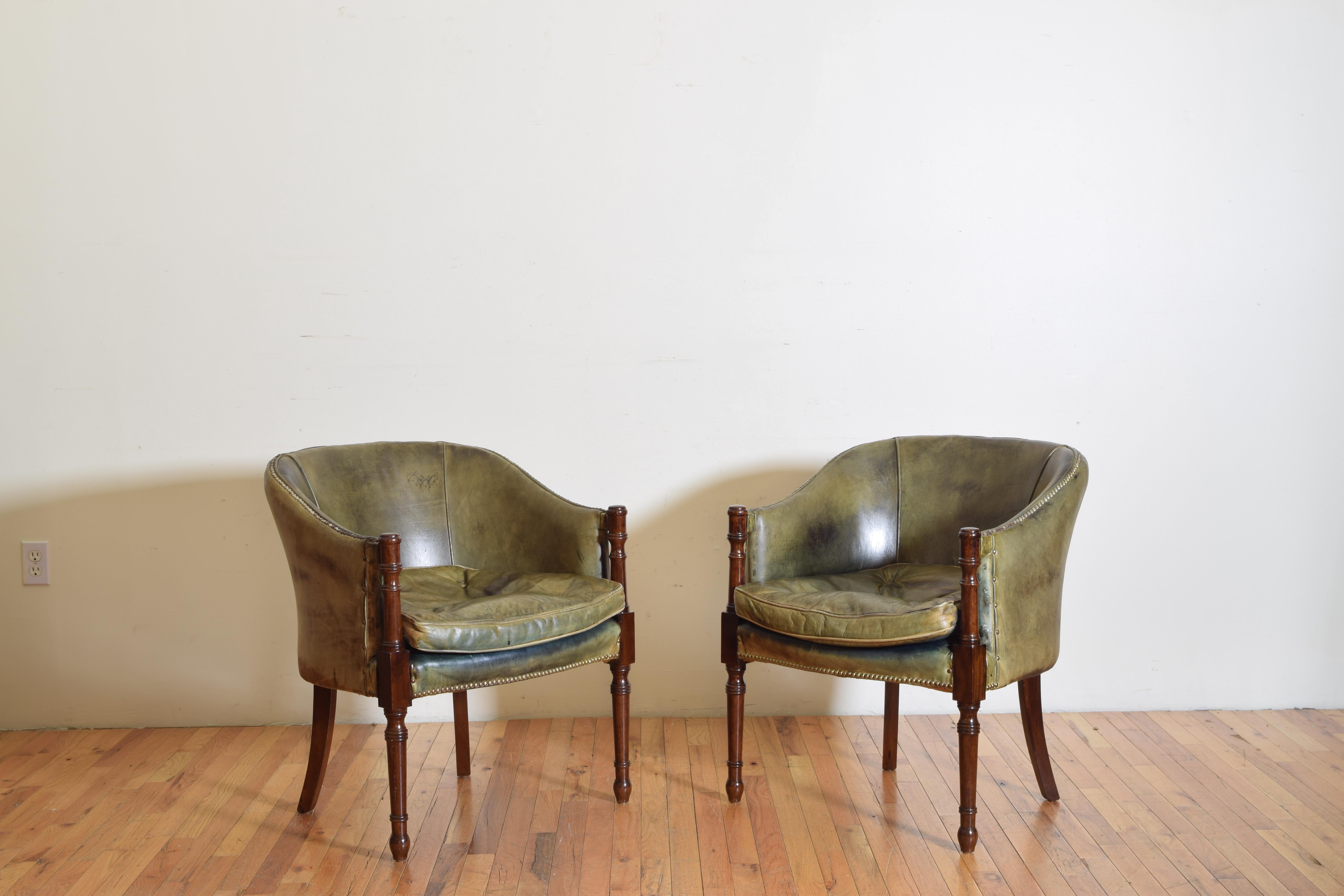 Upholstered in green leather, each having a concave backrest curving towards the front where turned arms supports continue to circular tapering legs, the back legs splayed, having loose down filled cushions.