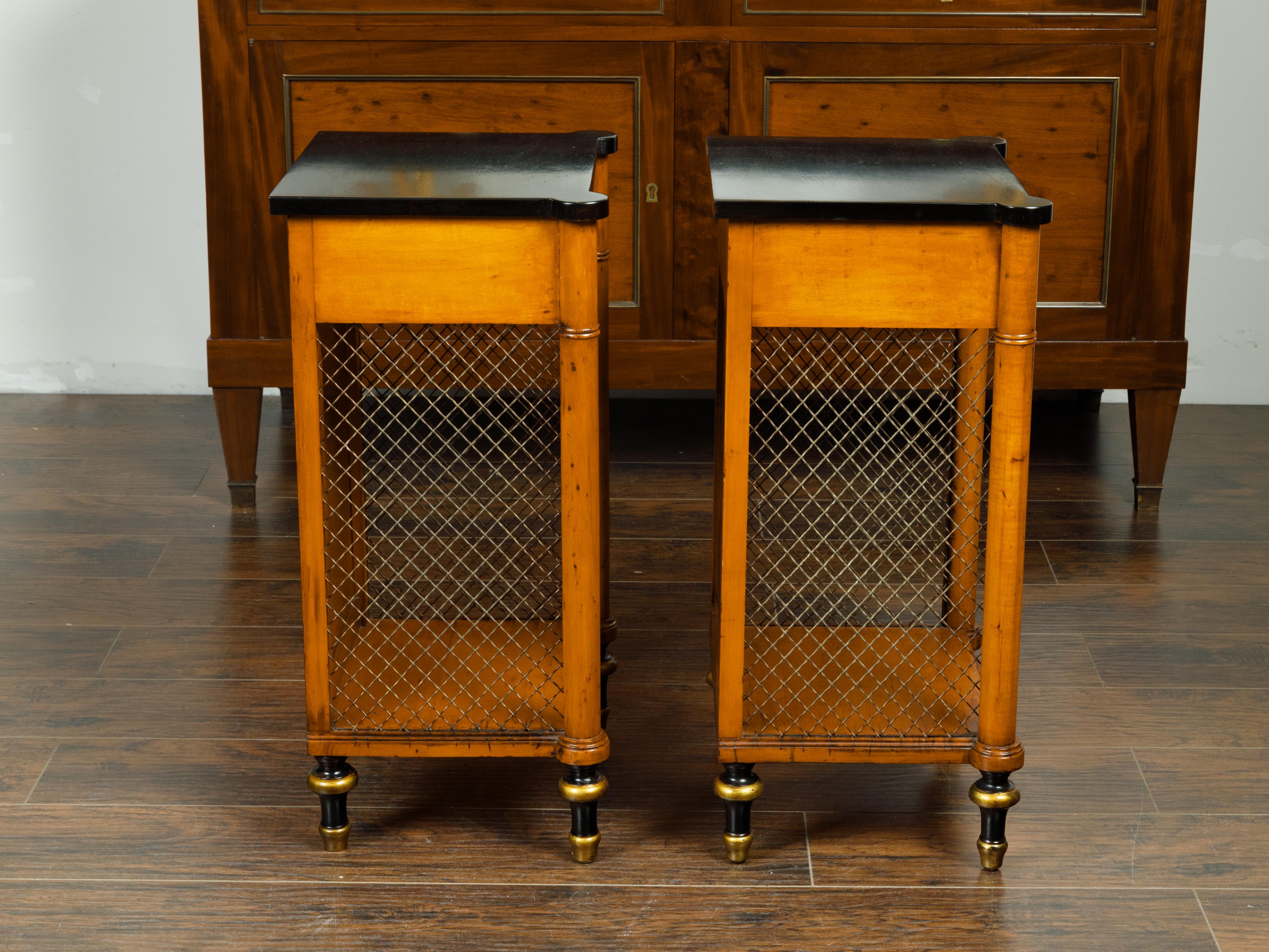 A pair of English Regency style walnut end tables from the mid 20th century, with ebonized tops, single drawer and chicken wire sides. Created in England during the midcentury period, each of this pair of Regency style end tables features a