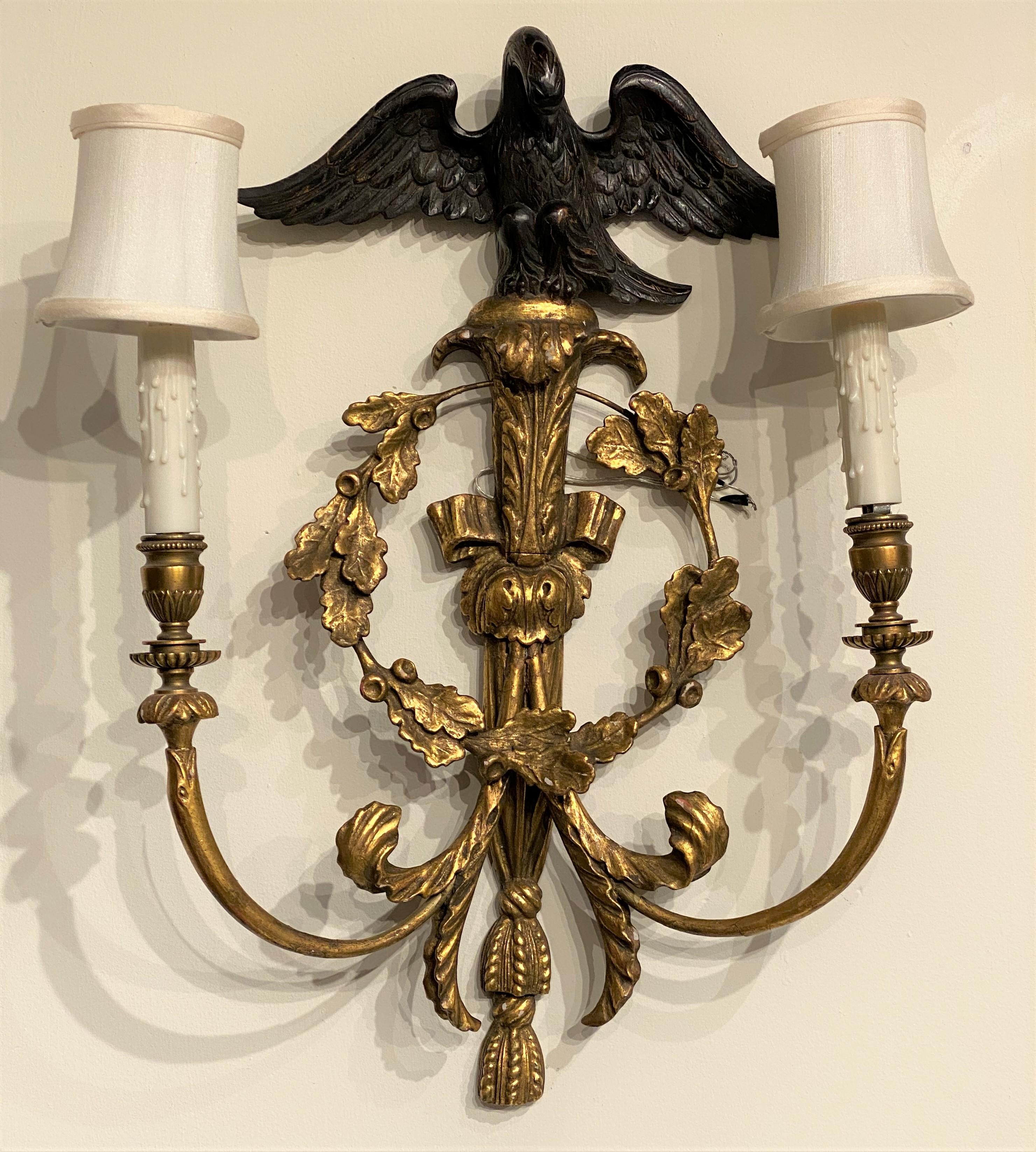 A fine pair of English Rococo style carved giltwood two-light sconces with metal arms, ebonized eagle tops and wreath motif. The pair dates to the 20th century and are in very good working order, recently rewired, with minor gilt gesso losses, and
