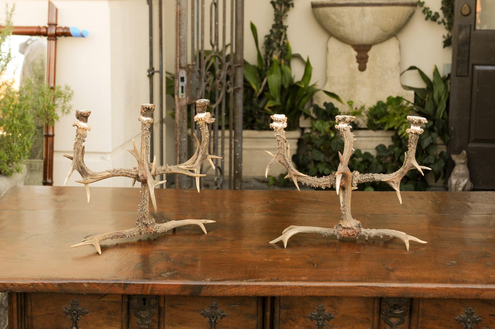 This pair of English rustic antler three-arm candelabra, dating from the 1940s, showcases the enchanting allure of countryside elegance and traditional craftsmanship. Each candelabrum is artfully composed of natural antlers, thoughtfully arranged to