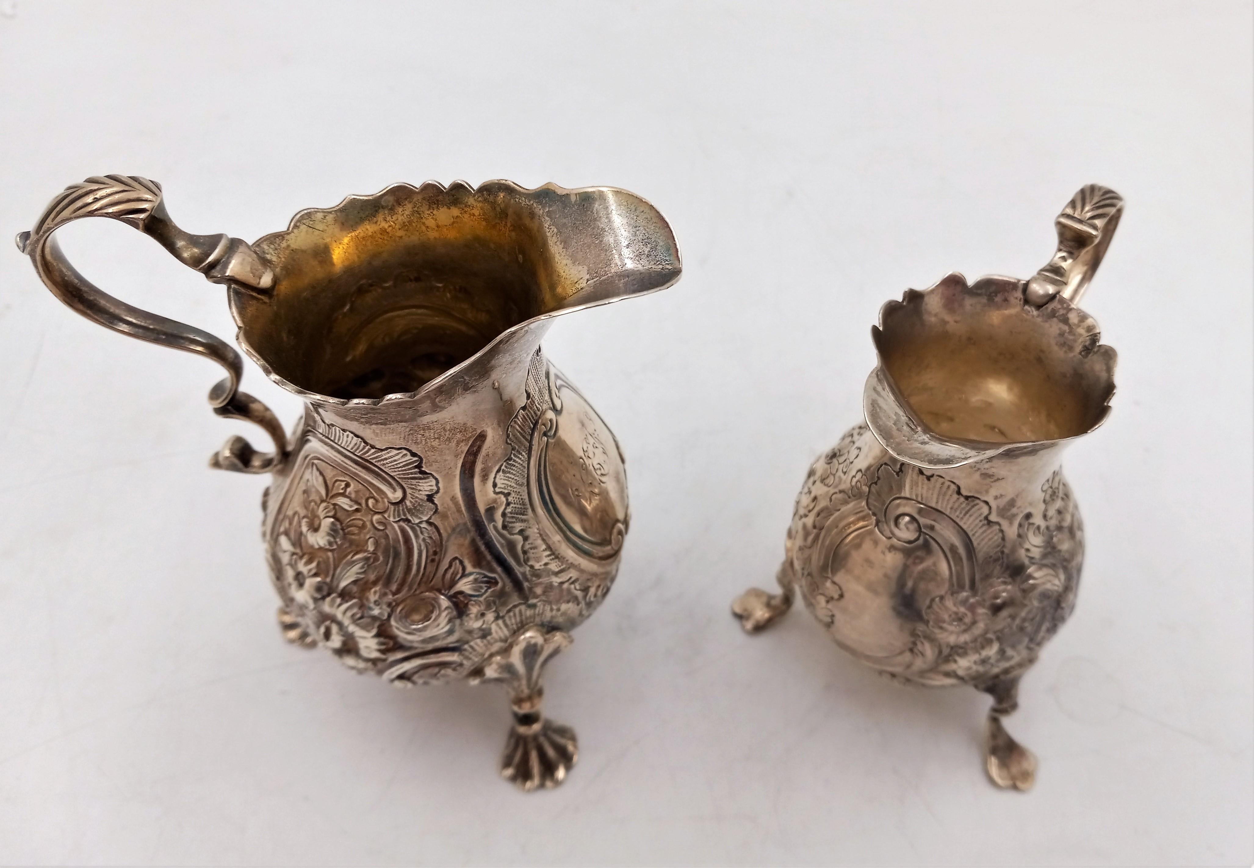 Pair of English Silver Georgian Cream Pitchers standing on shell legs and adorned in a floral pattern, circa mid-1800s. The larger of these two pieces is 4 3/4