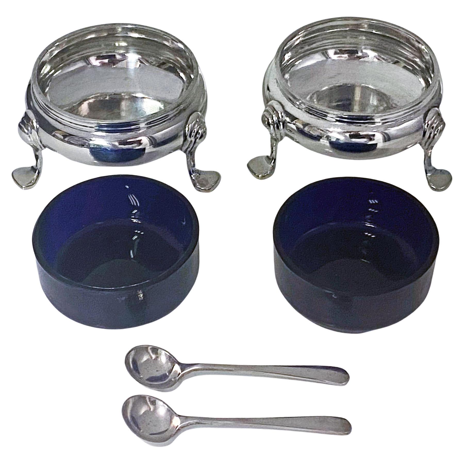 Pair of English Silver Georgian style open salts and spoons, cobalt blue liners, London 1968 Wakely and Wheeler. The salts of circular plain form with three turned supports, matching salt spoons and cobalt blue glass liners. Height: 1.25 inches.