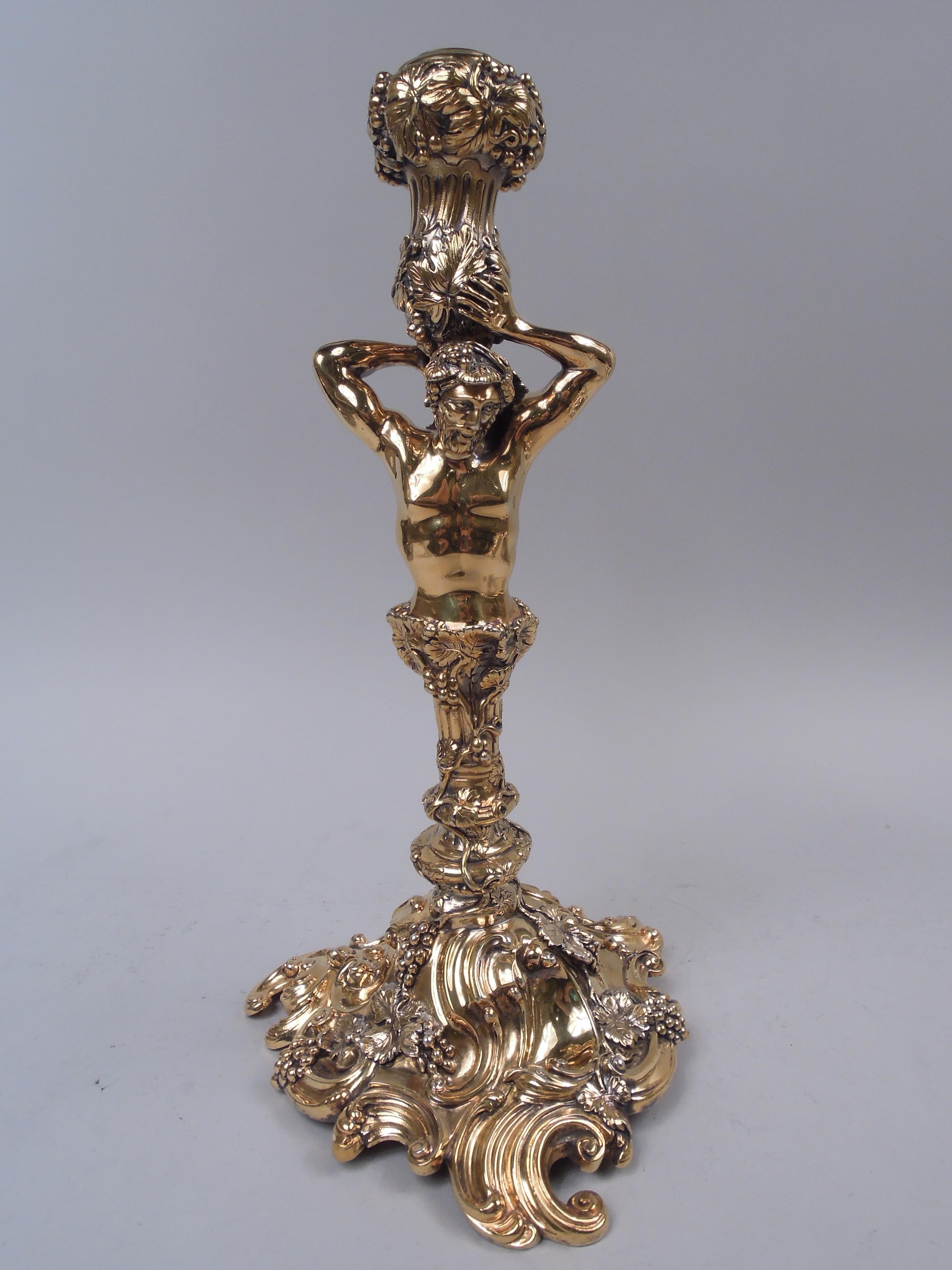 Pair of Georgian Rococo gilt sterling silver candlesticks, 1913. Each: Herm with muscular arms supporting elongated socket with twisted fluting and turned-down rim. Knopped columnar shaft on domed and scrolled foot. Wrap-around and entwined fruiting