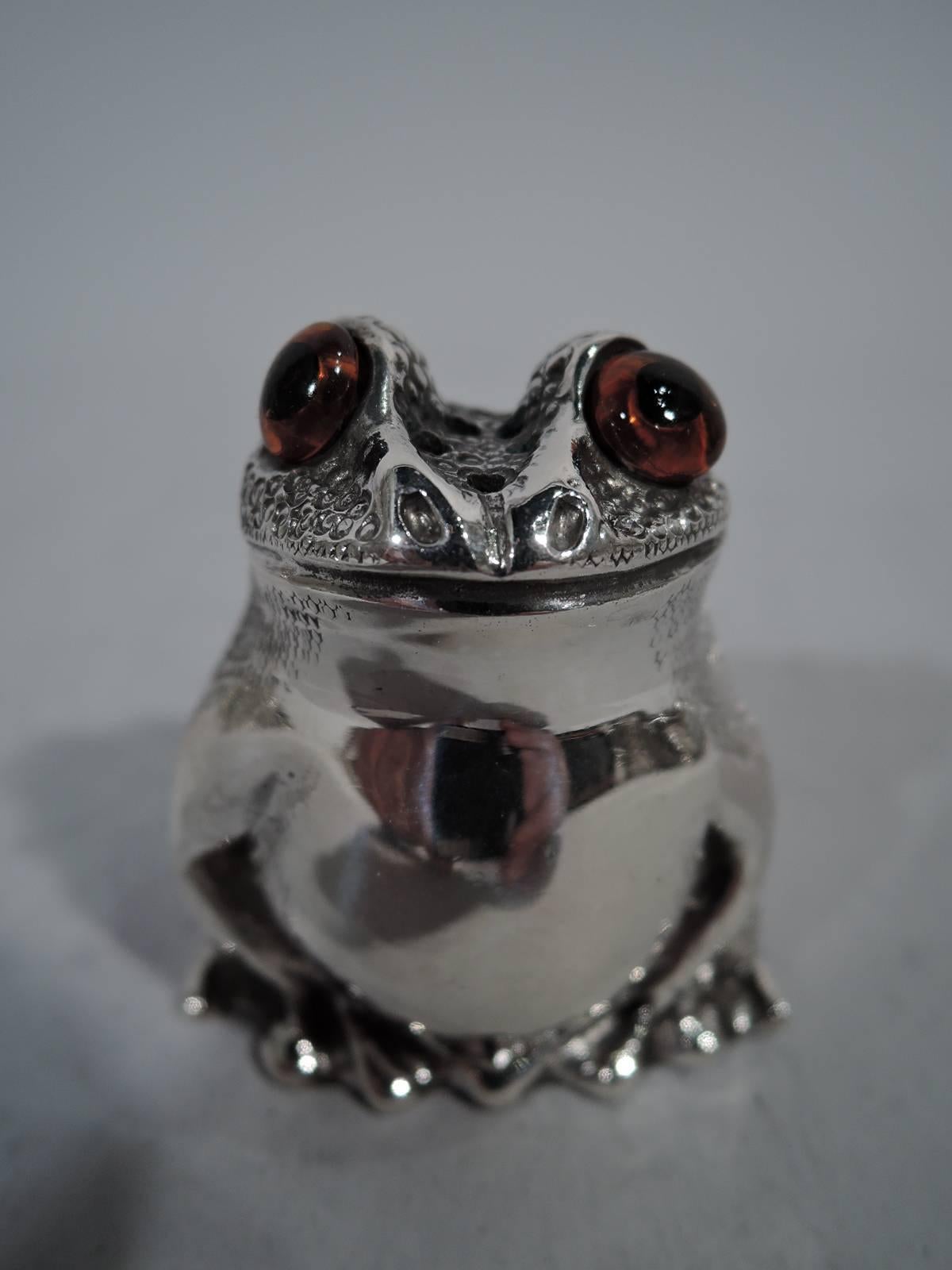 Pair of English sterling silver figural salt and pepper shakers. Each: A squatting reptile with legs gathered close to body. Scaly back, smooth front, and intense glass exophthalmic eyes. Closed mouth set in smirking smile. One has plastic plug; the