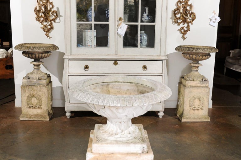 A pair of English stone garden urns on pedestals from the 20th century with laurel wreaths and gadroon motifs. Created in England during the 20th century, each of this pair of garden urns features a circular beveled lip adorned with ovoid motifs,