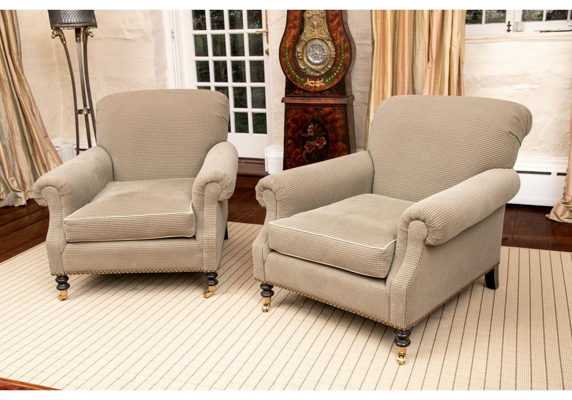 A Pair of larger and very comfortable Club chairs with sloping scrolled backs and scrolled arms. Raised n ebonized turned front legs on casters and square splayed back legs. Finely upholstered in a small taupe and grayish green check fabric with