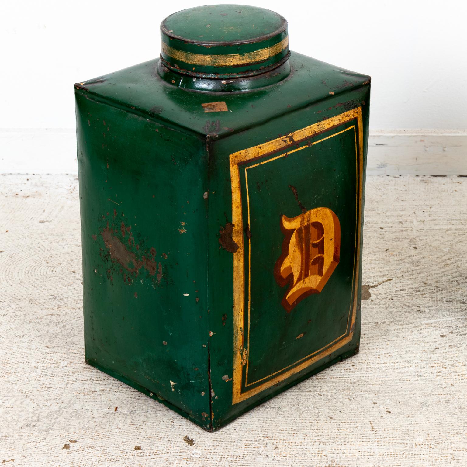 Circa 1880s pair of English tea canisters in tin. The canisters feature a green painted surface with gilded 