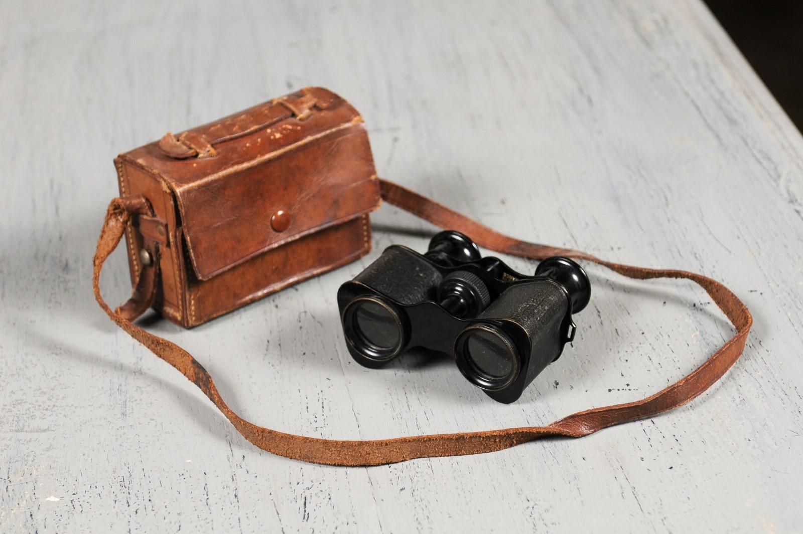 A pair of English Turn of the century binoculars from the early 20th century displayed in their original leather case. Born in England at the very end of Queen Victoria's reign, this pair of binoculars have made it all the way to us protected by