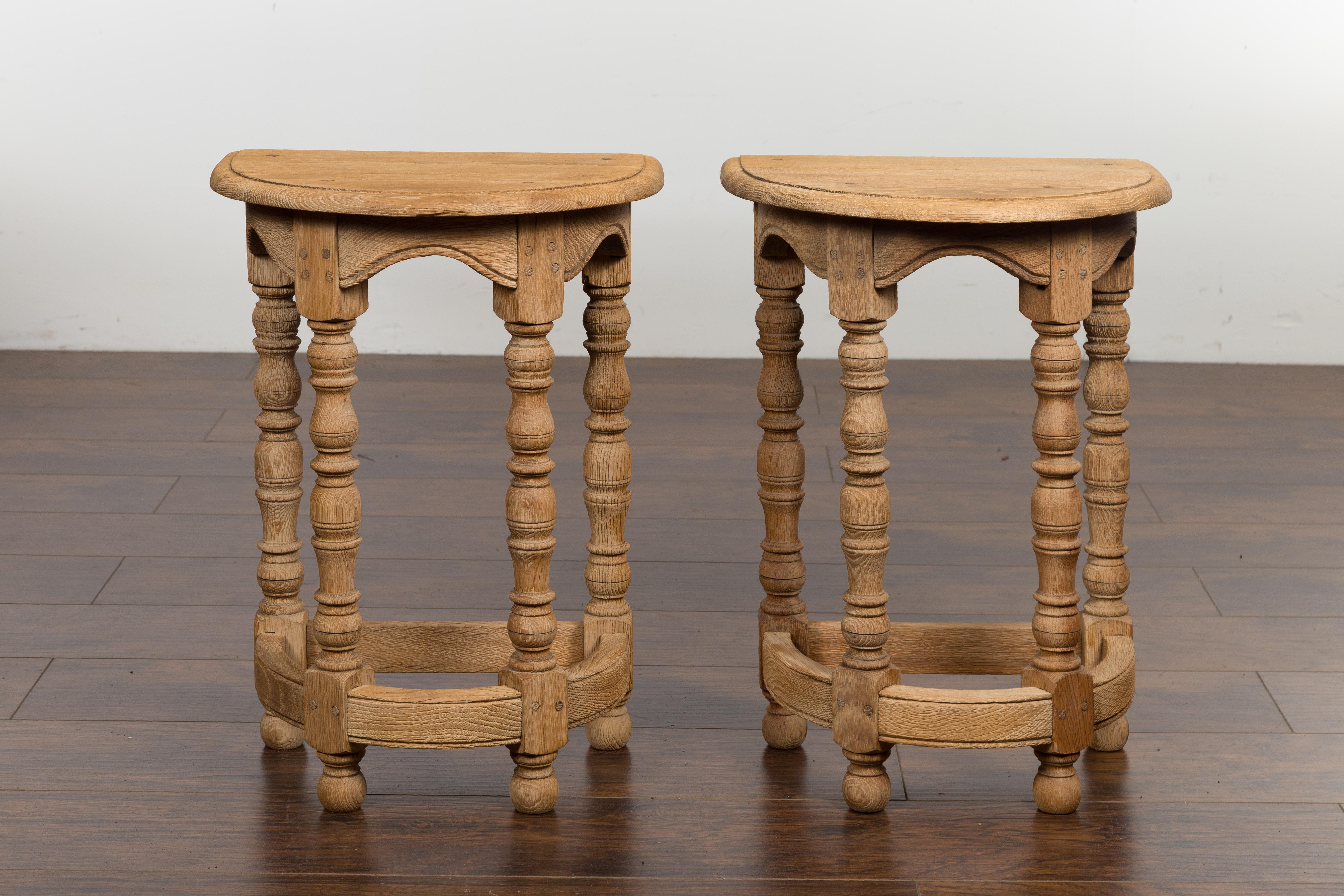 A pair of English bleached stools from the early 20th century, with turned legs and semi-circular tops. Created in England during the turn of the century, each of this pair of stools features a semi-circular top sitting above four turned legs