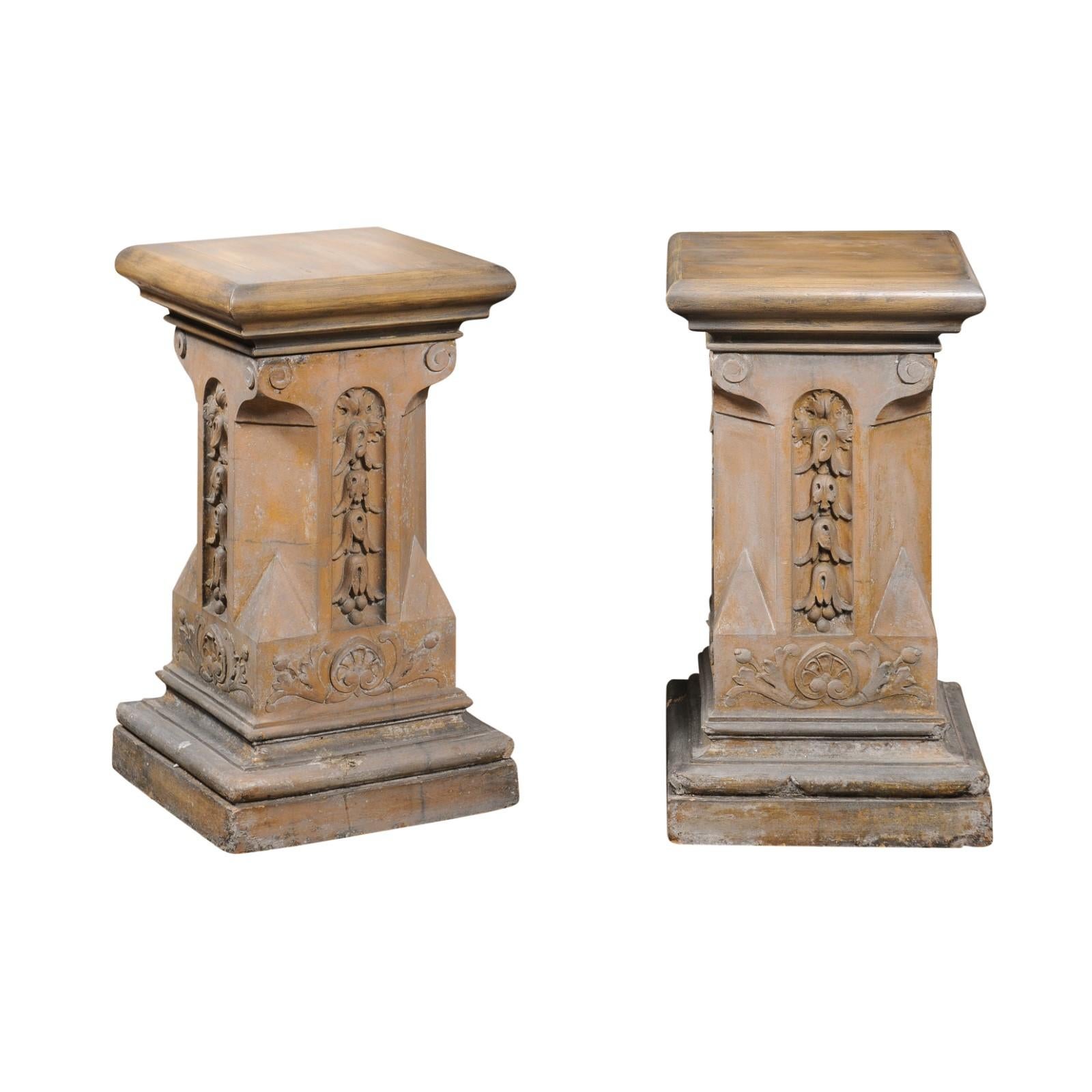 A pair of English Victorian period terracotta pedestals from the late 19th century with campanula, foliage and volute motifs on square bases. Created in England during the long reign of Queen Victoria in the third quarter of the 19th century, each