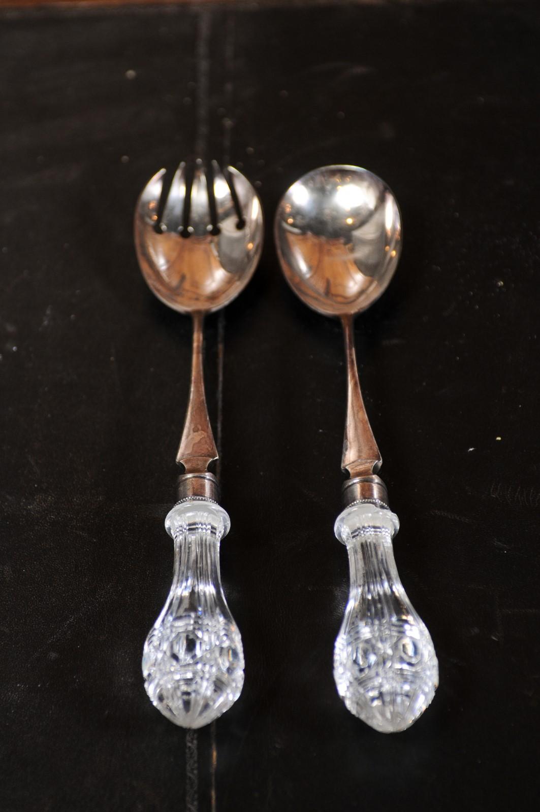 A pair of English Victorian period fine silver serving spoons from the 19th century, with glass handles. Created in England during the reign of Queen Victoria, each of this pair of serving spoons is adorned with a cut glass handle perfectly