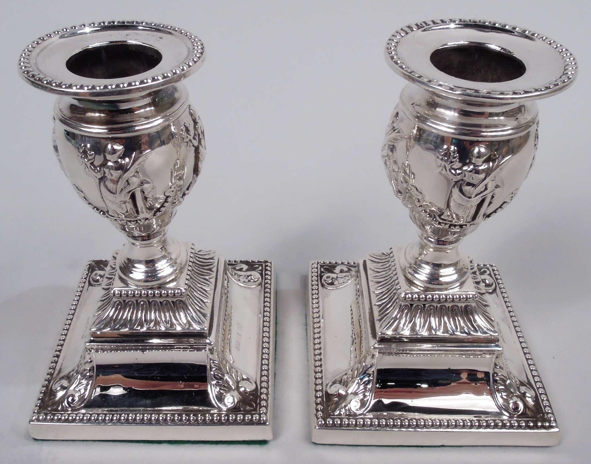 Pair of Victorian Classical sterling silver low candlesticks. Made by Richard Hodd & Son in London in 1881. Each: Ovoid socket with bobeche on spool support mounted to stepped square base with scrolling leaves at corners. In low relief draped