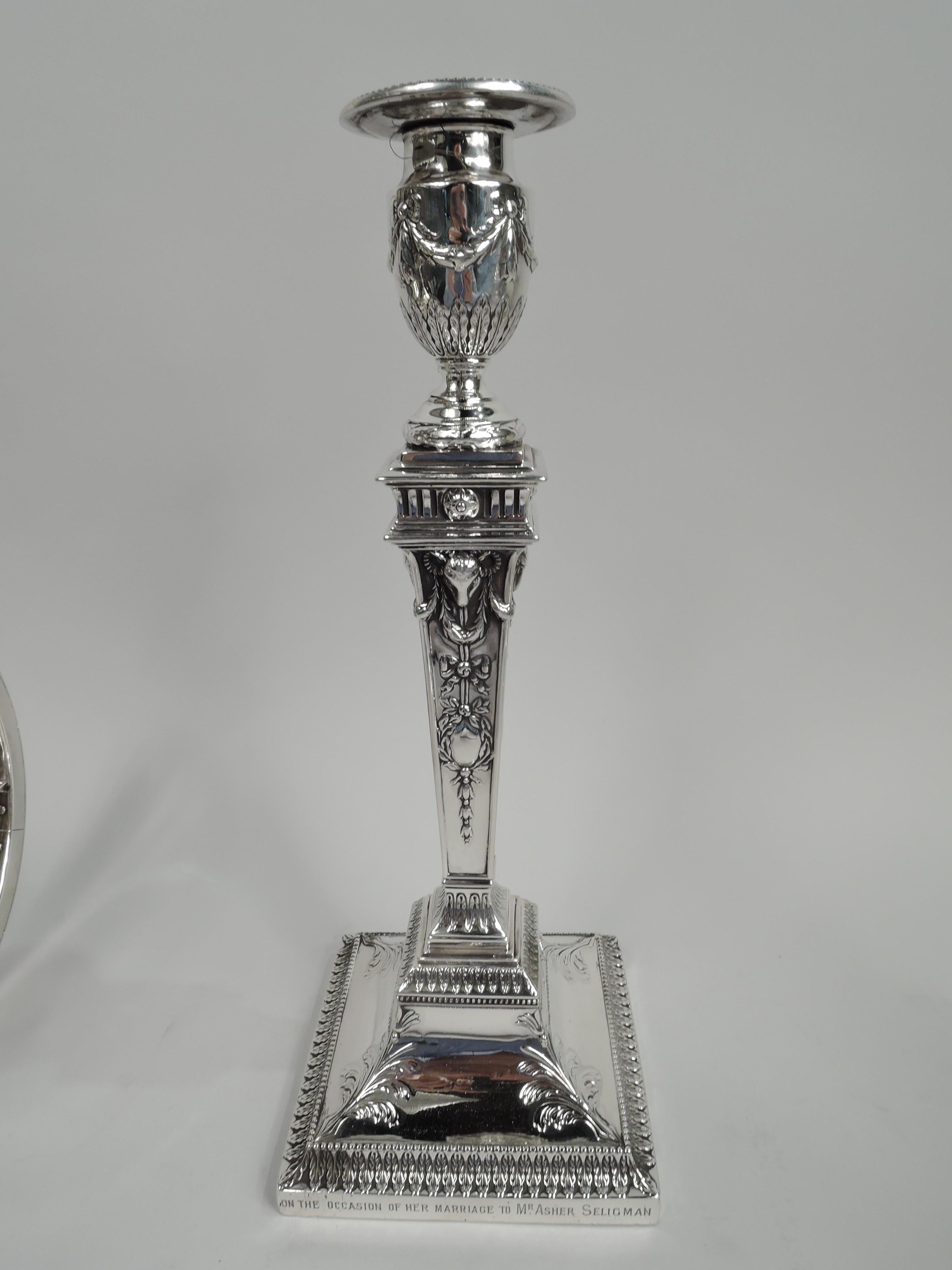 Pair of Victorian neoclassical sterling silver candlesticks. Made by Hawksworth, Eyre & Co., Ltd in Sheffield in 1880-1. Each: Urn socket on domed foot mounted to tapering pillar on raised square foot. Beading, leaf-and-dart, swags, and ram’s heads.