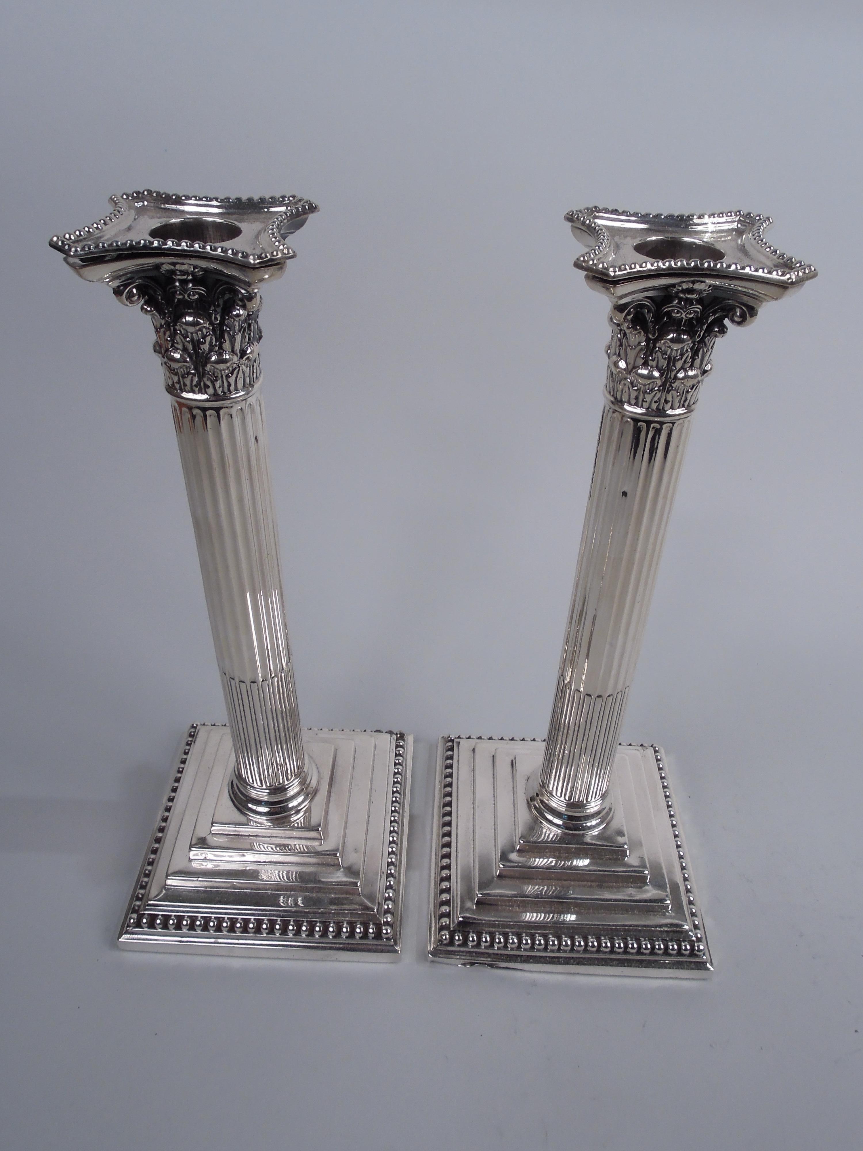 Pair of English Victorian Neoclassical sterling silver candlesticks. Made by William Hutton & Sons in London in 1889. Each: Traditional column with stop-fluted shaft on stepped square foot. Composite Corinthian capital with concave sides and