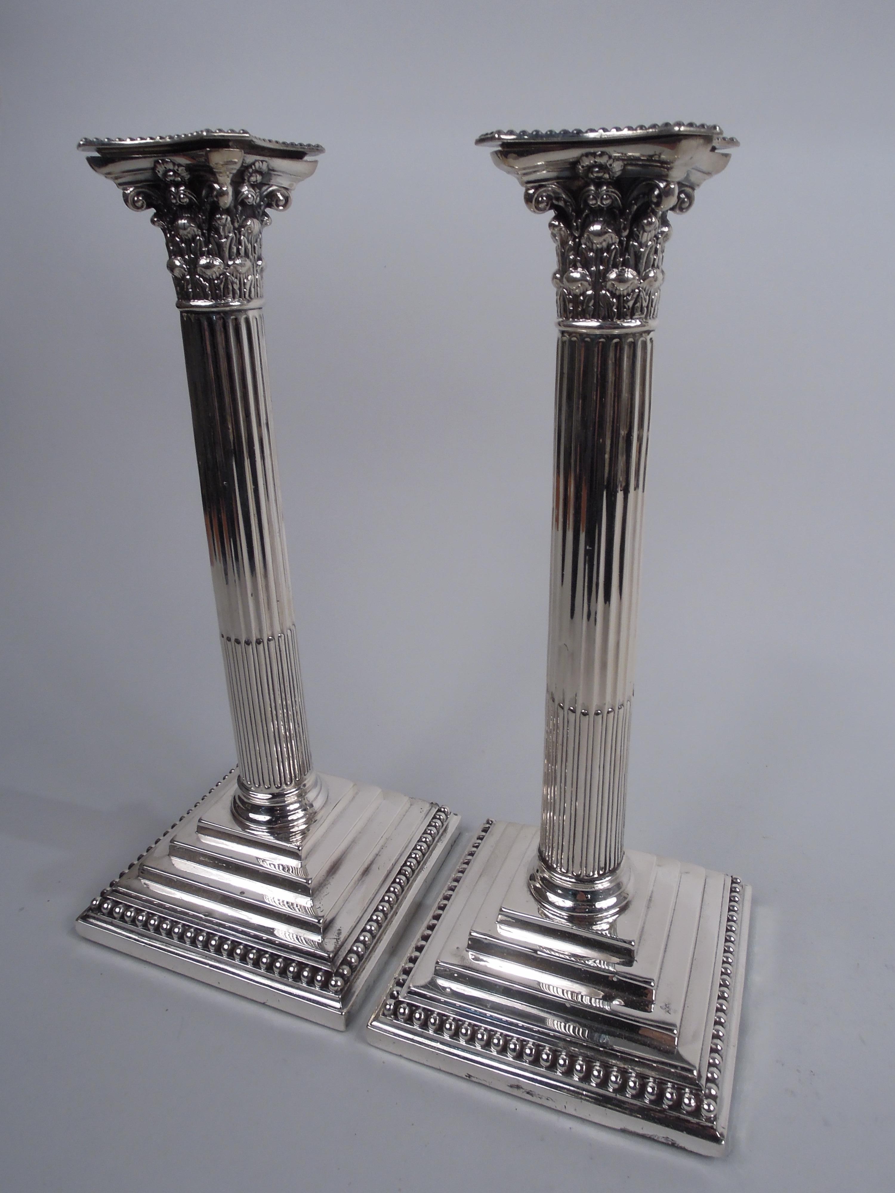 Pair of English Victorian Neoclassical sterling silver candlesticks. Made by William Hutton & Sons in London in 1889. Each: Traditional column with stop-fluted shaft on stepped square foot. Composite Corinthian capital with concave sides and