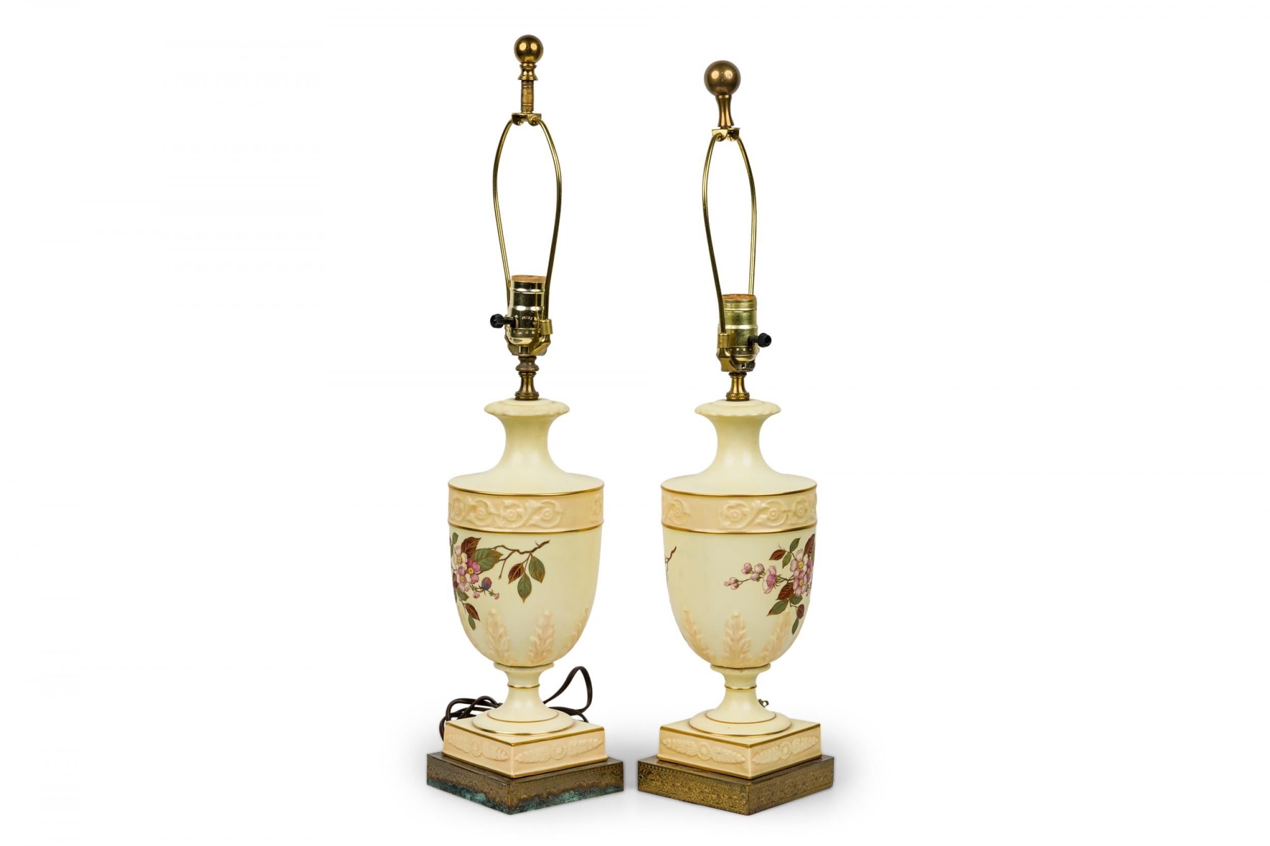 Pair of English Victorian style (late 20th century) table lamps with white ceramic urn-form bodies with painted floral designs, resting on a square base and mounted with brass hardware. (Priced as pair).