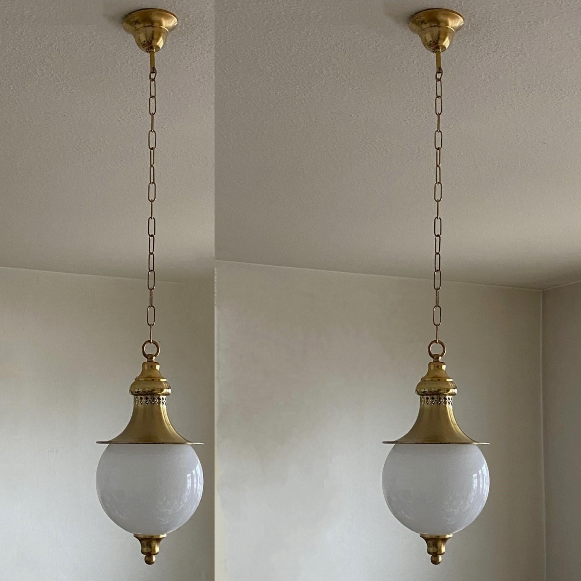 A beautiful and rare pair of hand-blown opaline glass ceiling pendants with brass gallery, England circa 1930.
Most unusual opaline glass ball with finial underneath brass shade with pierced details for light projection.
Brass with wear commensurate