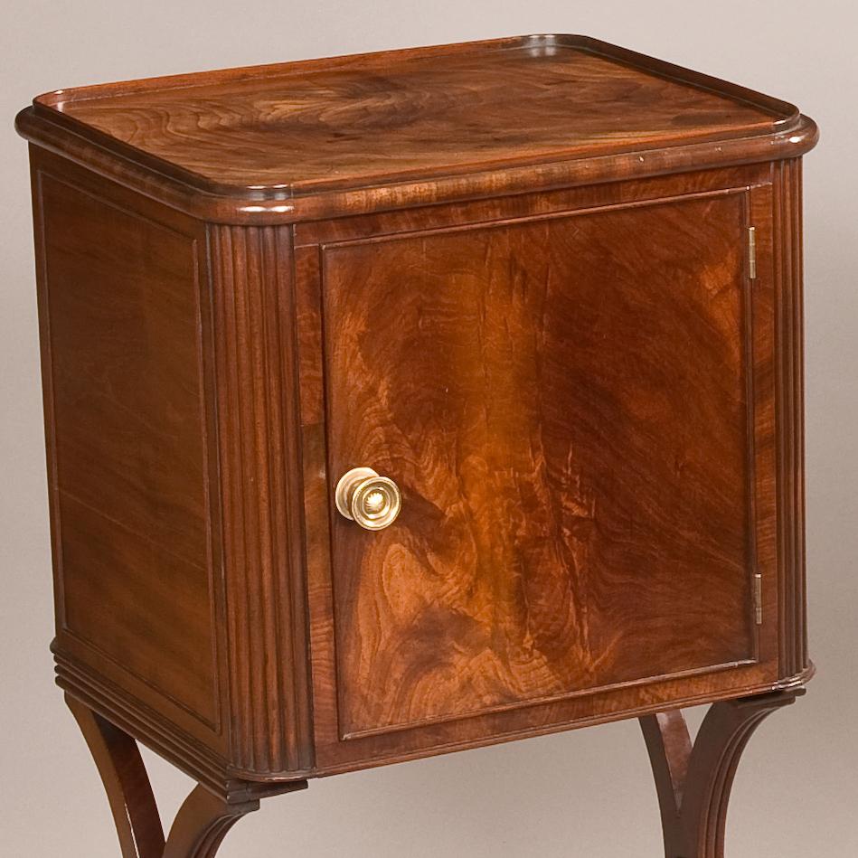 An attractive pair of bedside cupboards of the Regency period

Constructed in mahogany, rising from an end support base of scrolled ‘X’ form, with a tapering and turned stretcher, having exterior reeded bosses, the whole rising from oblong