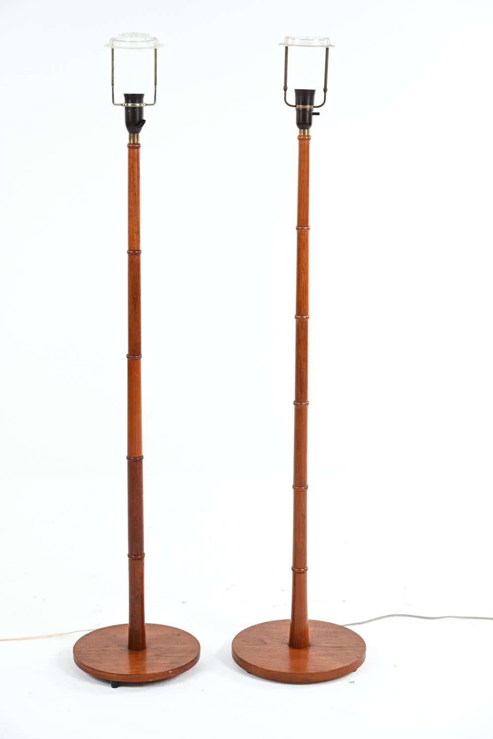 A pair of Scandinavian modern floor lamps in delicate turned teak wood, with faux bamboo rings and round bases. Designed c. 1950's-60's by Esben Klint for Le Klint, this simple yet stylish pair of lamps have slightly different socket fittings. No