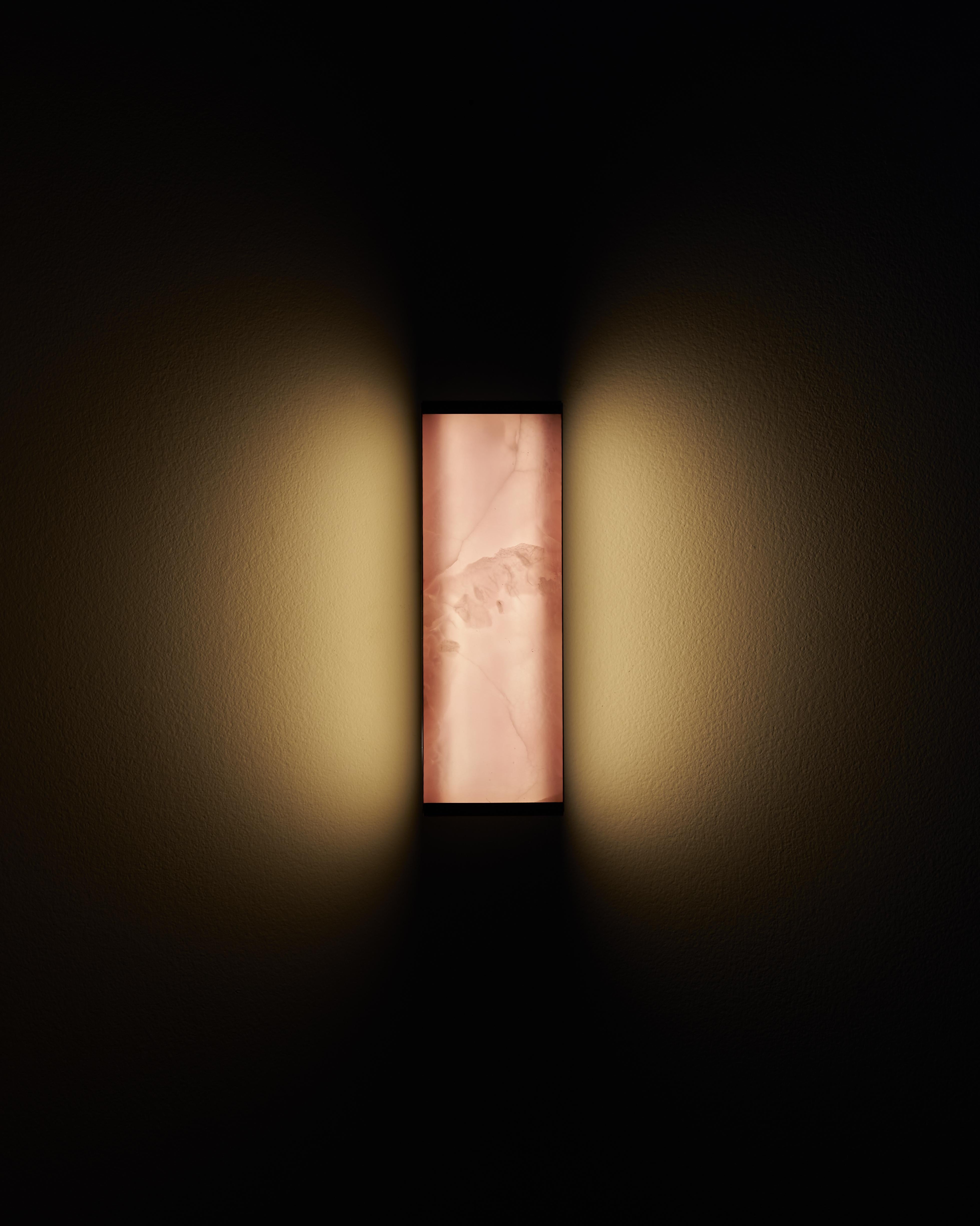 Die Tech Short Wall Sconce ist eine Leuchte, bei der Leuchte und Lampenschirm nahtlos zu einer Einheit verschmelzen. Sie nutzt die lichtdurchlässigen Eigenschaften von ultradünnem Onyx, um ein Wechselspiel von Licht und Schatten zu erzeugen, das die